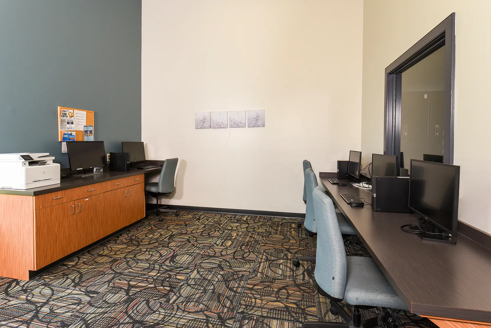 Modern communal office space with sleek computer stations, stylish furniture, and vibrant patterned carpet.