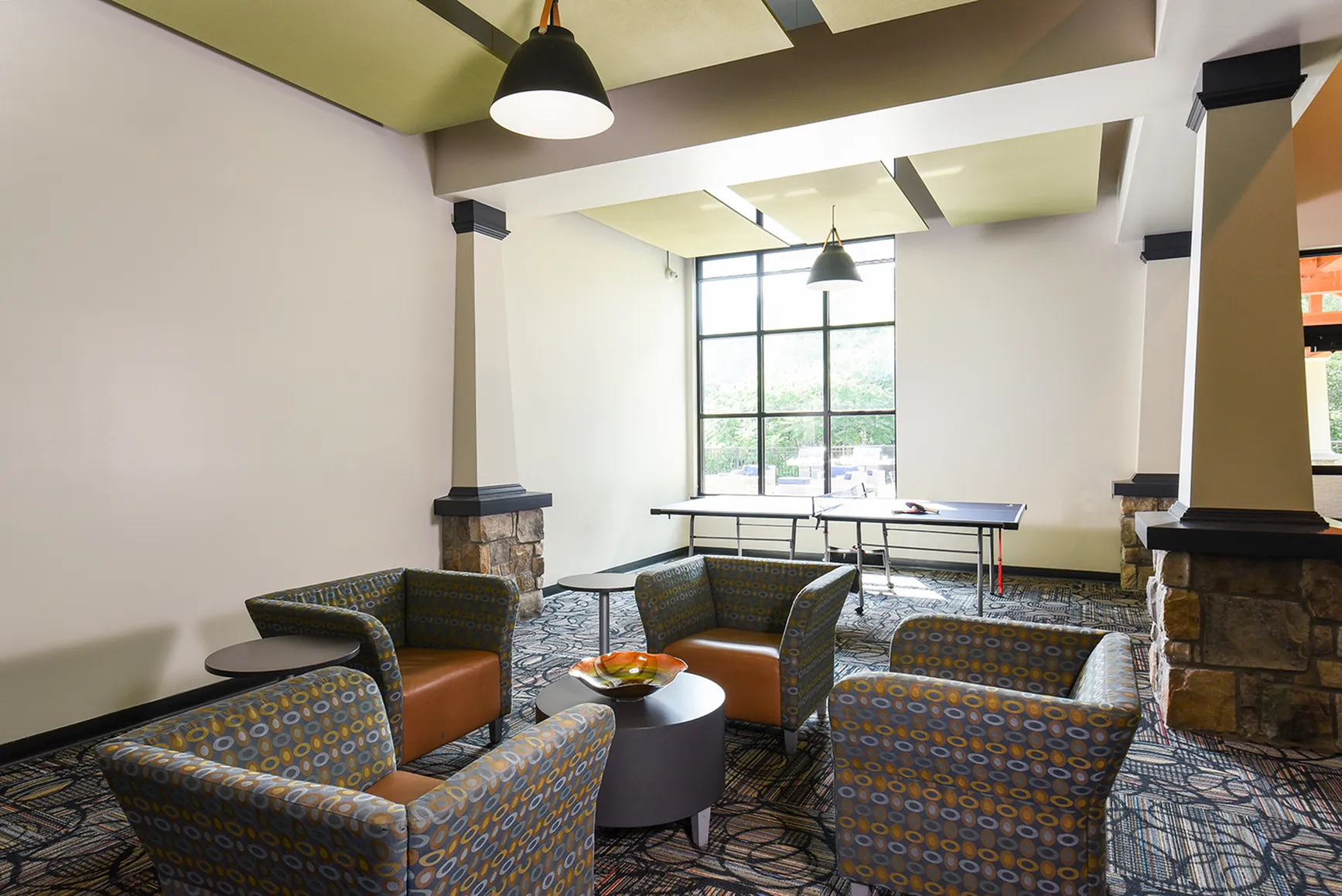 Inviting modern lounge area with stylish patterned armchairs, large windows, and a ping pong table, exuding comfort and leisure.