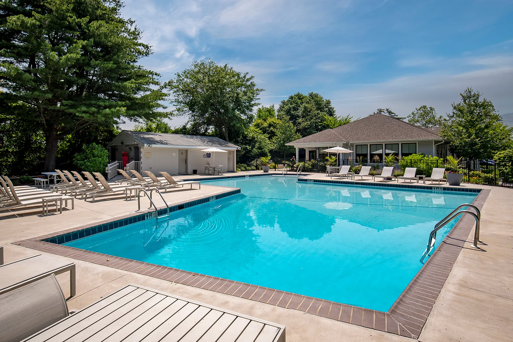 Luxurious outdoor pool area with elegant lounge chairs surrounded by lush greenery and a modern clubhouse.
