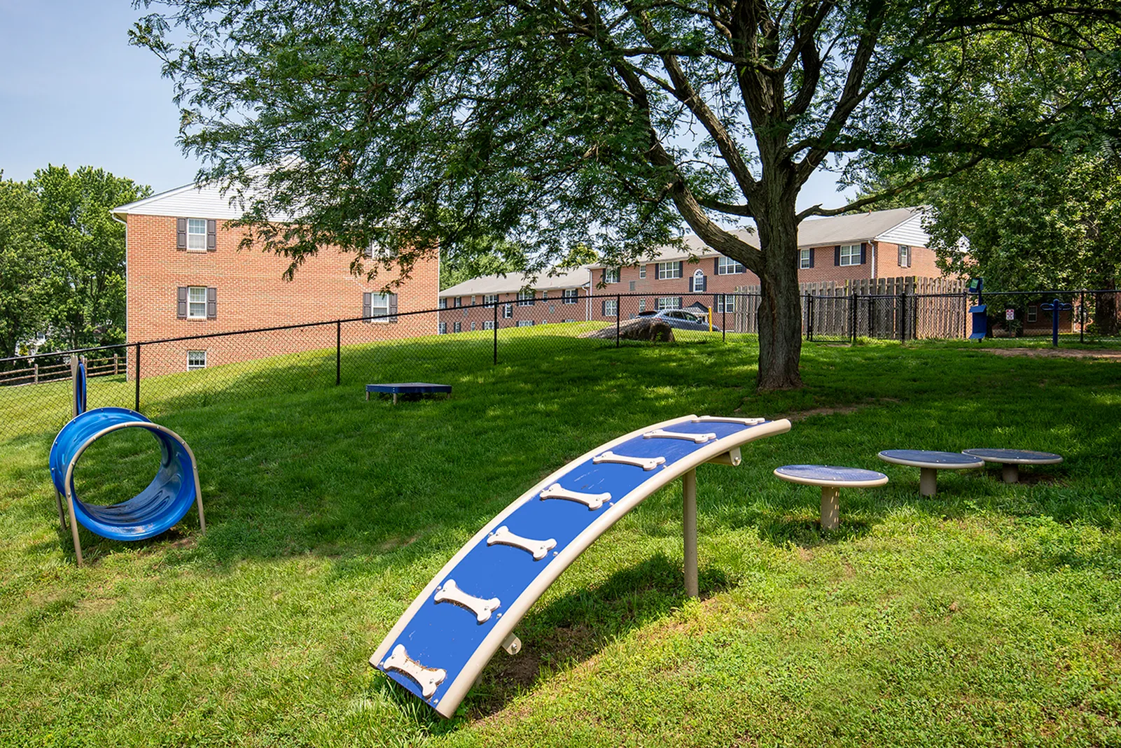 Inviting playground area nestled within a lush green apartment community, featuring modern play structures under the shade of a majestic tree.