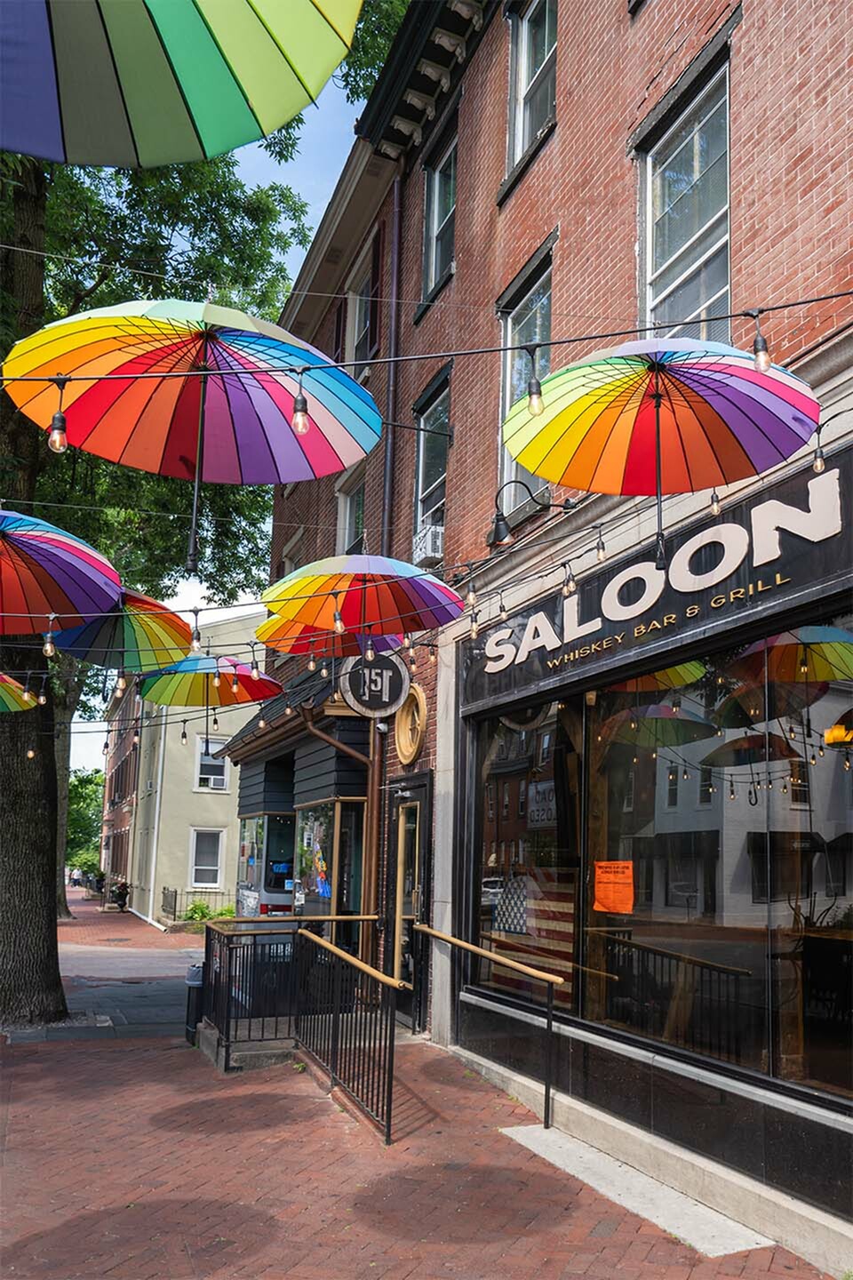 Charming street view featuring a vibrant whiskey bar and grill, adorned with colorful umbrellas hanging above the sidewalk, creating a lively and inviting atmosphere.