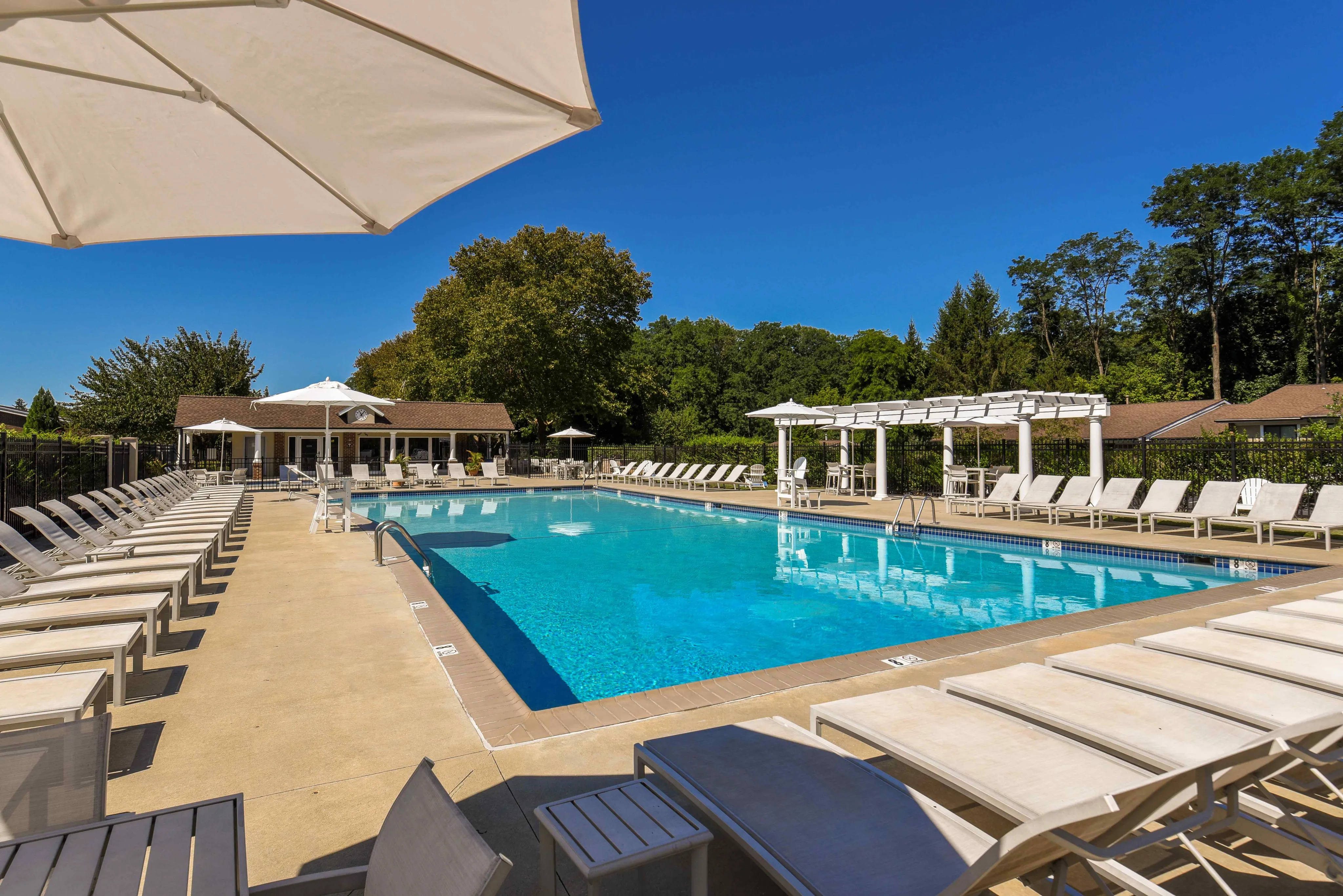 Luxurious outdoor pool area with abundant lounge chairs, surrounded by lush greenery and a bright blue sky, perfect for relaxation and leisure.