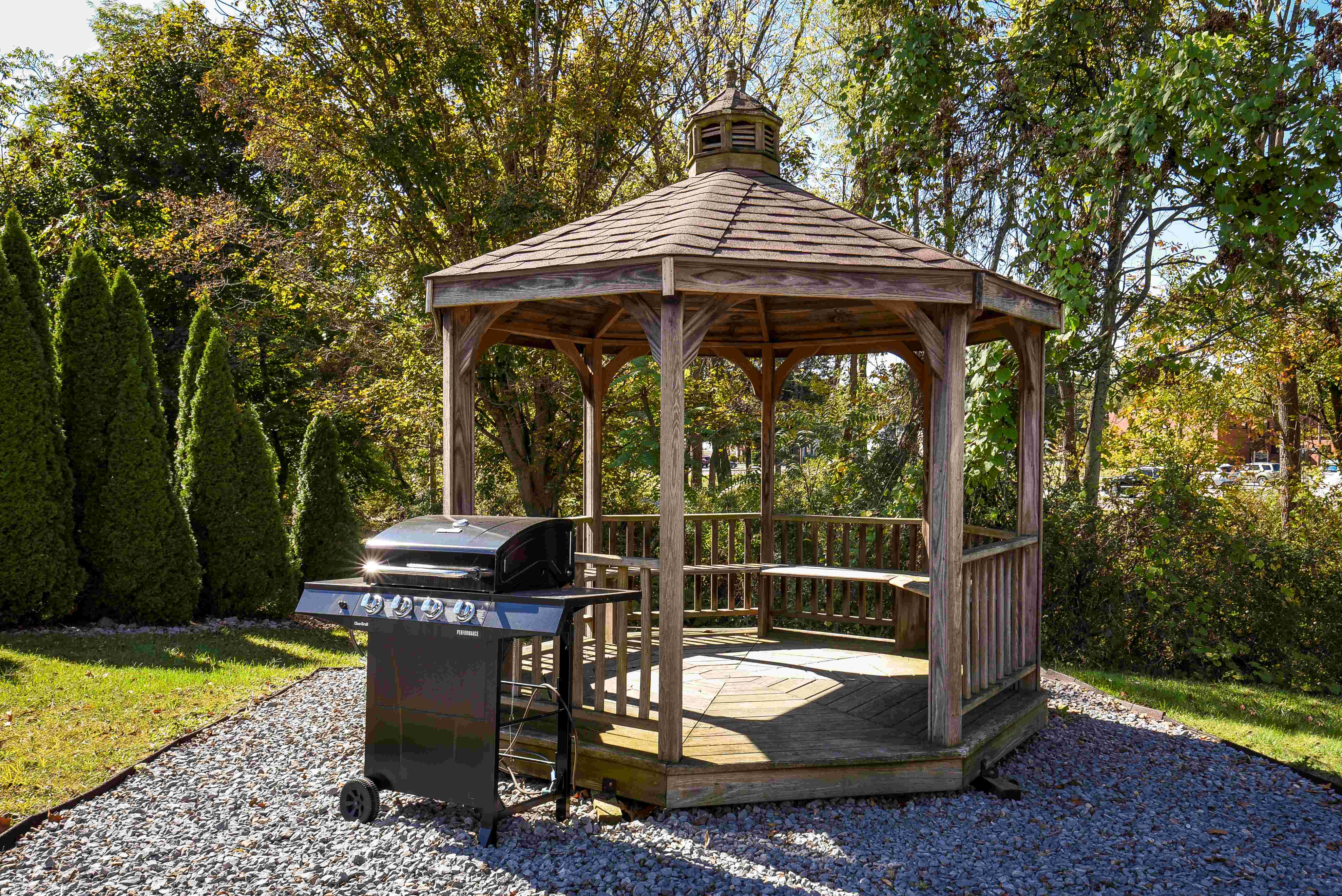Charming wooden gazebo nestled in a lush green garden with a modern barbecue grill, perfect for outdoor gatherings and relaxation.