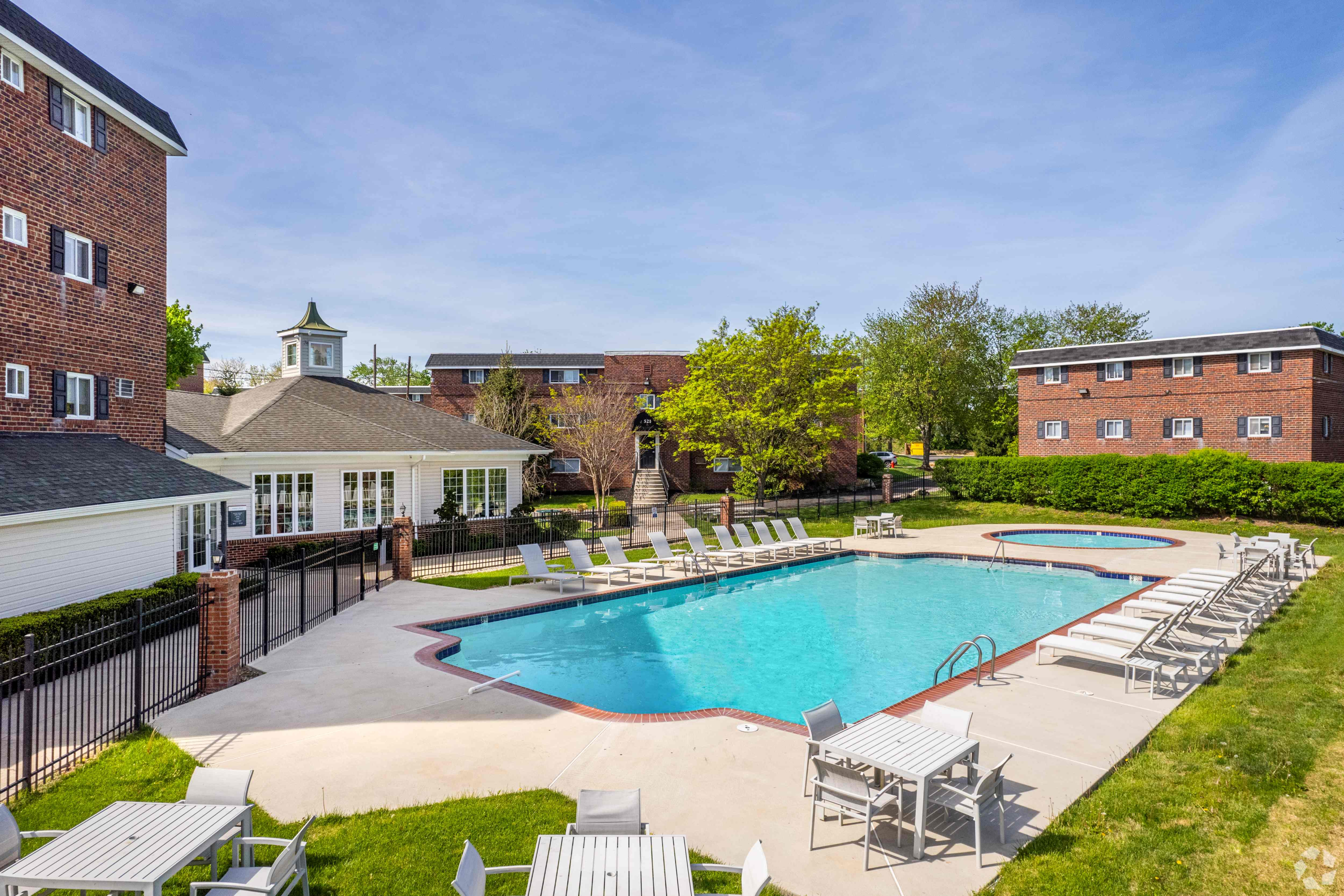 Charming residential pool area with lounge chairs, surrounded by lush greenery and brick buildings, perfect for relaxation and leisure.