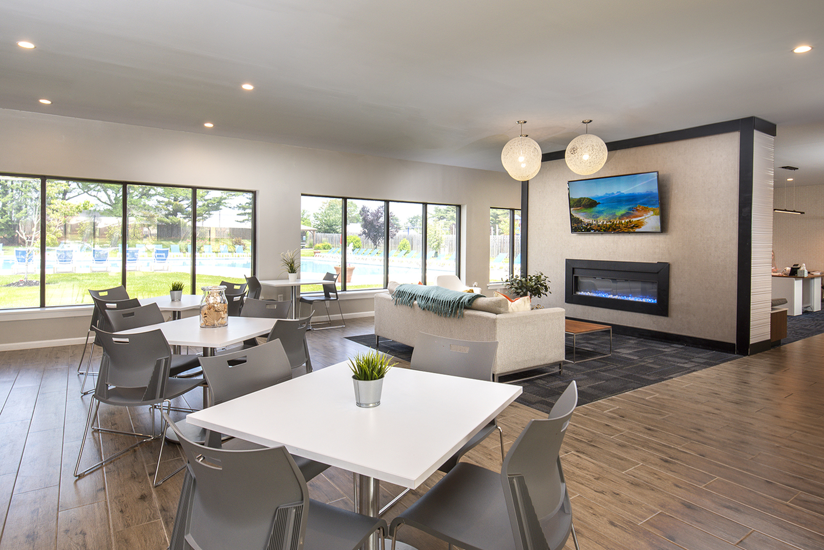 Modern communal lounge with large windows overlooking a pool, featuring stylish seating, vibrant decor, and a sleek fireplace.