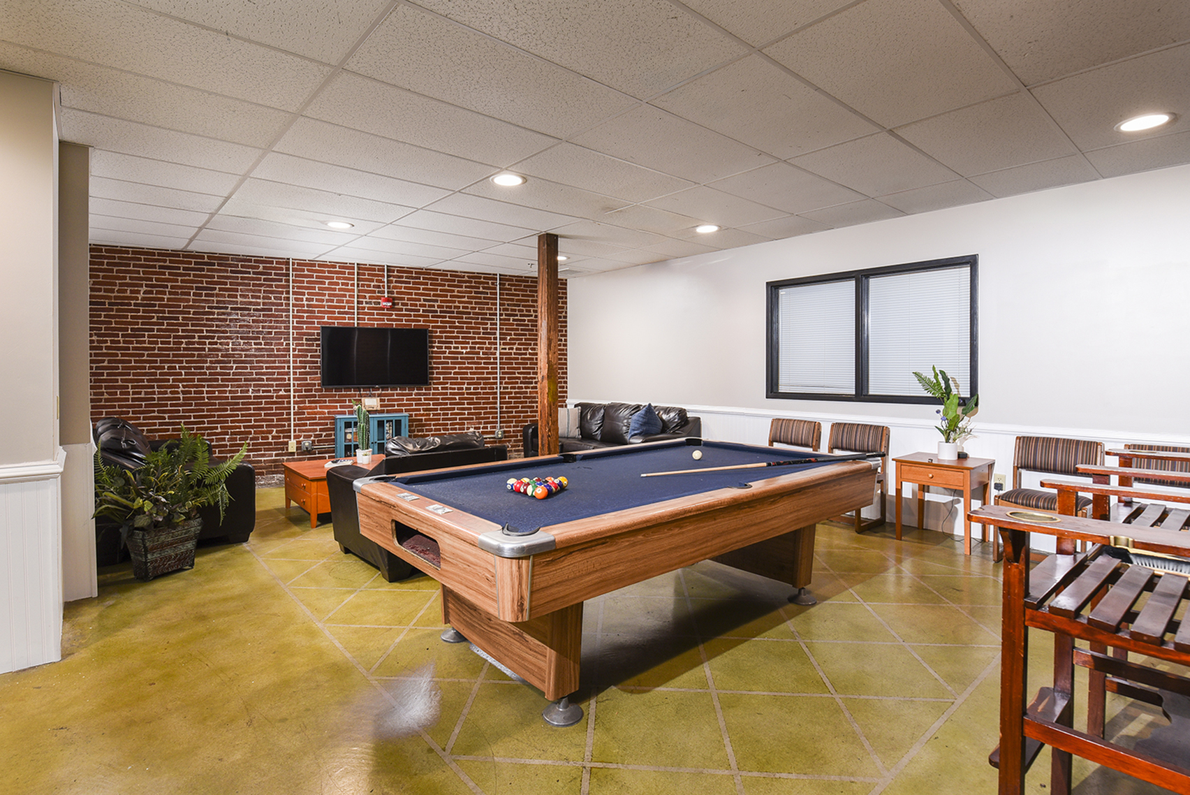 Chic game room with a pool table, cozy seating, and a modern TV setup against a stylish brick accent wall.
