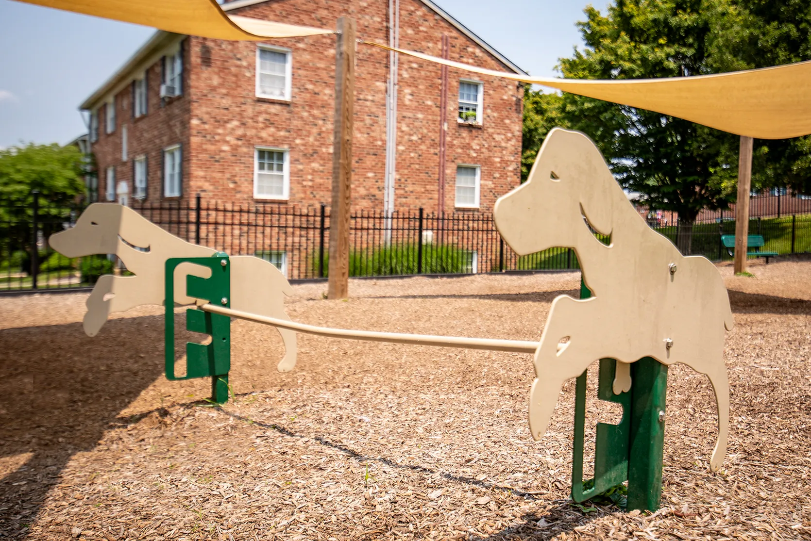 Charming playground featuring dog-shaped seesaws with a backdrop of a brick apartment building and lush greenery.