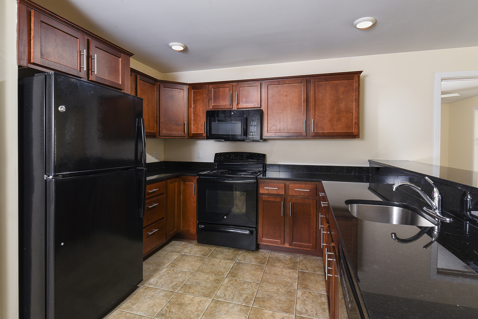 Elegant kitchen with dark granite countertops, rich wooden cabinets, and modern black appliances, offering a stylish and functional cooking space.