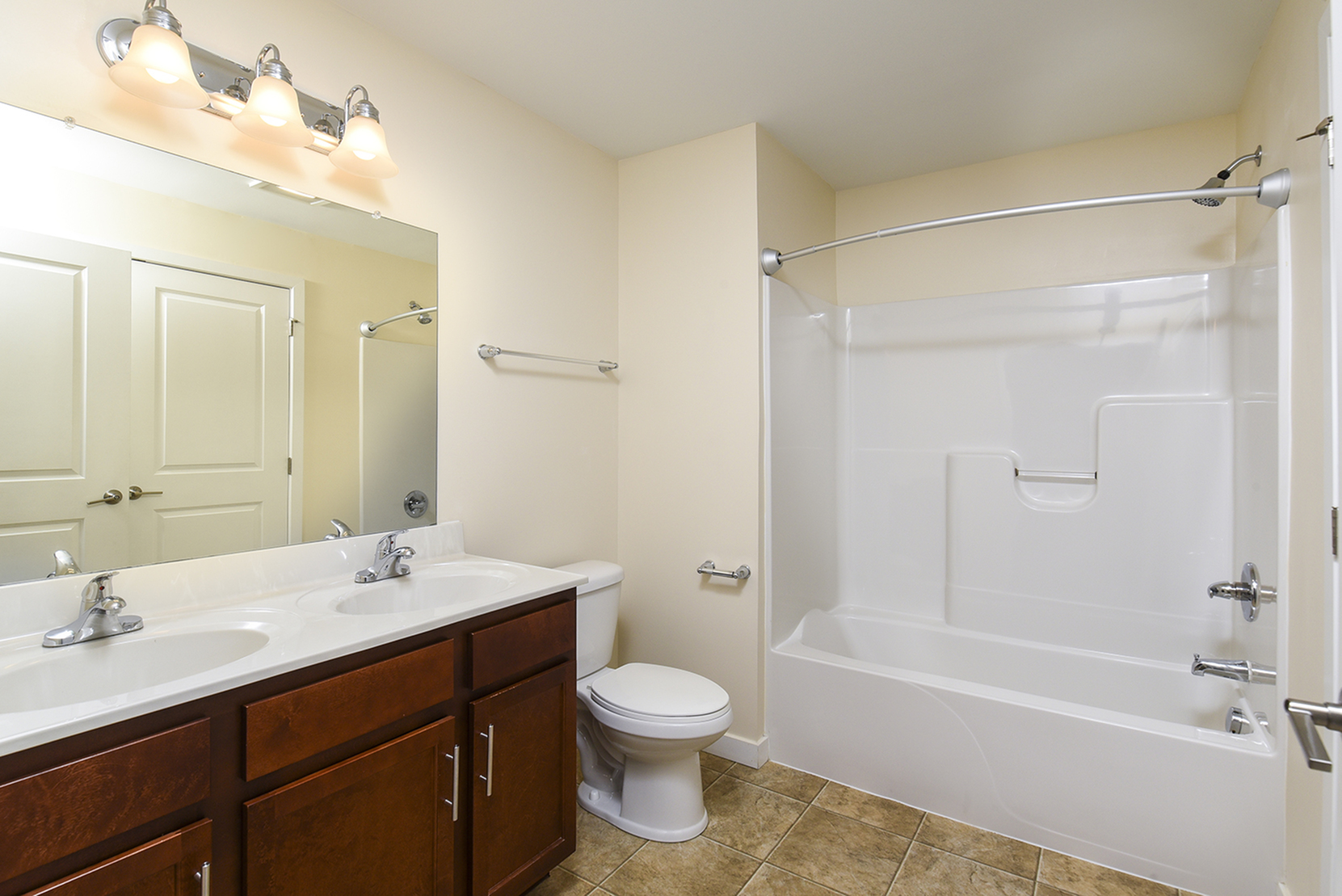 Modern bathroom featuring dual sinks, elegant lighting, and a spacious shower-tub combination.
