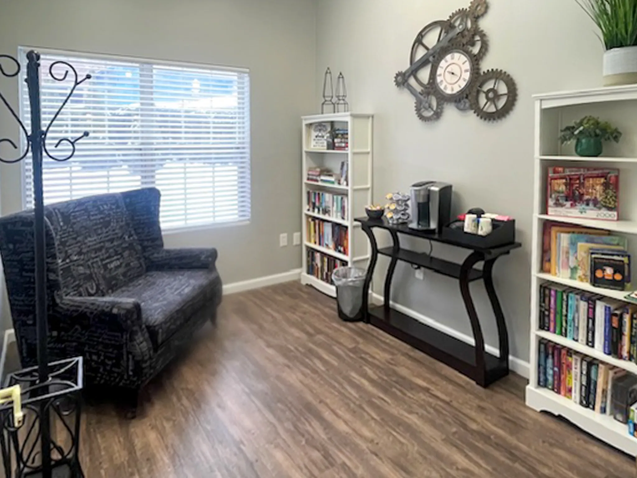 Cozy reading nook with a plush patterned sofa, stylish wall clock, coffee station, and book-filled shelves, perfect for relaxation and inspiration.