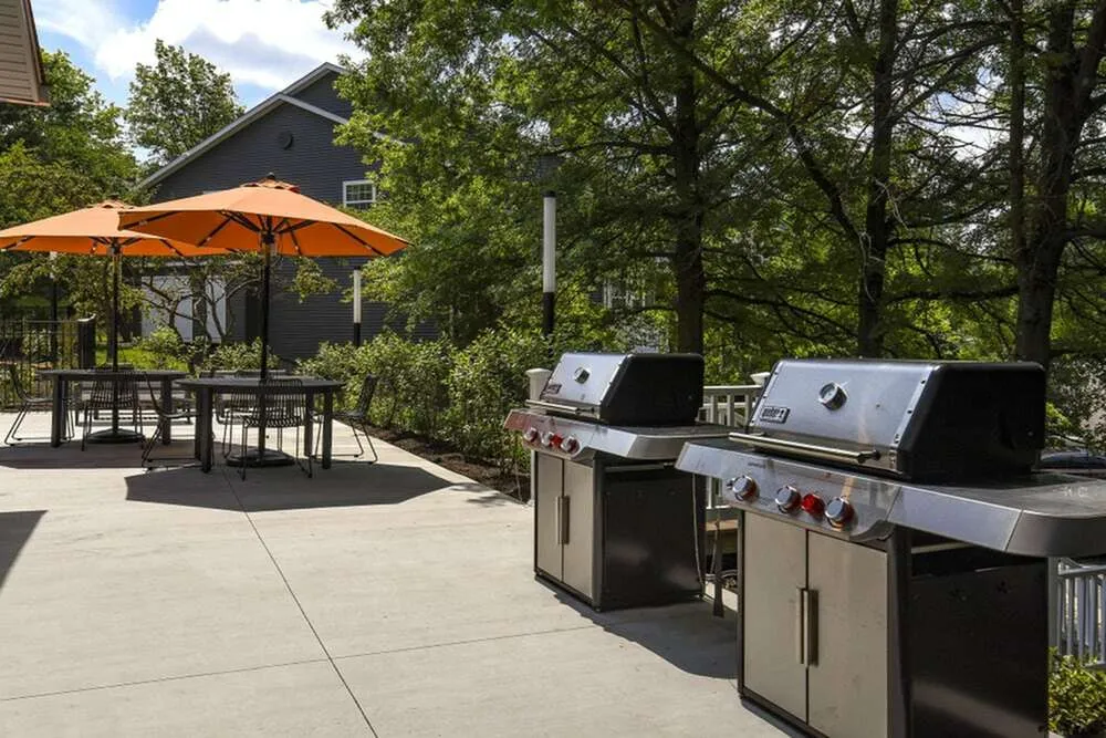 Charming outdoor patio with modern grills and vibrant orange umbrellas, perfect for entertaining guests amidst lush greenery.