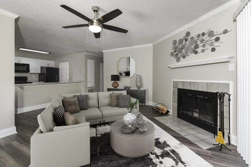 Elegant living room with cozy L-shaped sofa, modern ceiling fan, and charming fireplace, leading to an open kitchen for seamless entertaining.