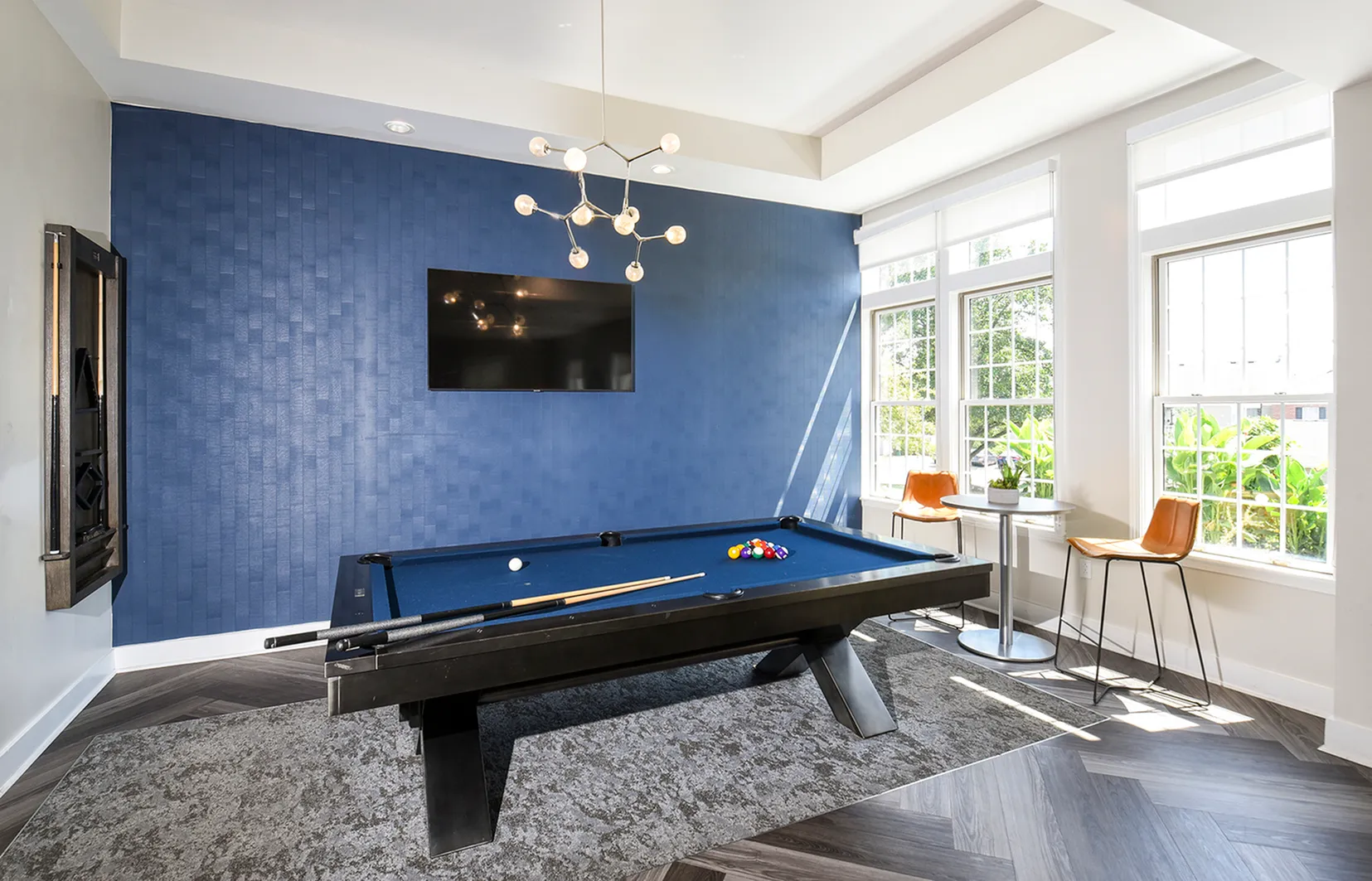 Bright and modern game room with a sleek pool table, stylish blue accent wall, and large windows offering abundant natural light.