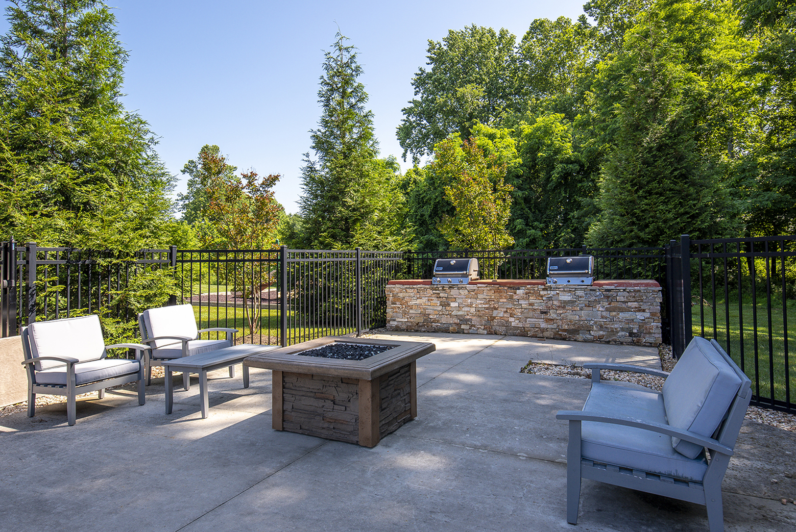 Charming outdoor patio with comfortable seating, a modern fire pit, and built-in grills surrounded by lush greenery.