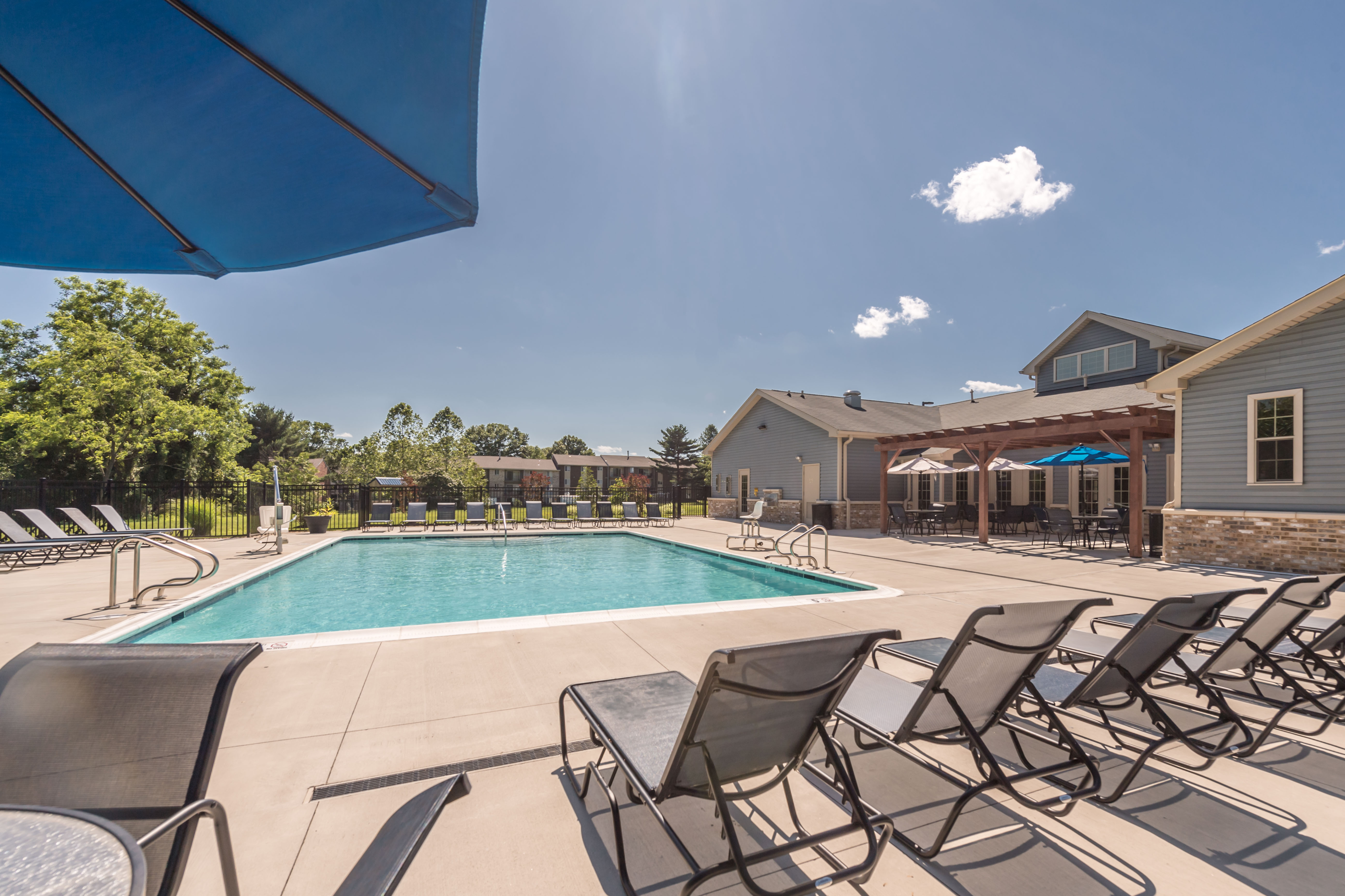 Inviting apartment complex featuring a sparkling swimming pool with stylish lounge chairs and covered seating area, perfect for relaxation and social gatherings.