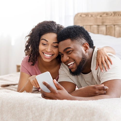 happy black couple using smartphone on bed