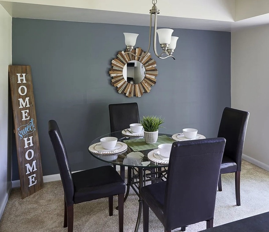 Dining room with table settings and glass dining table, black chairs, mirror on the wall and home sweet home sign in the corner