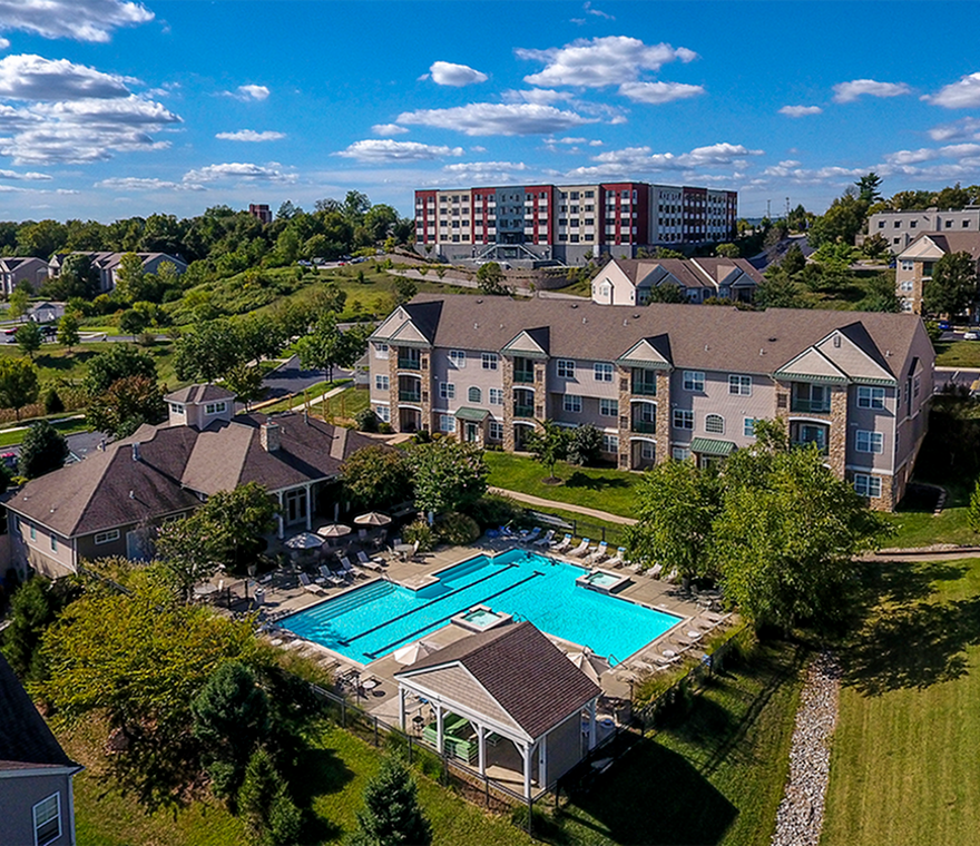 Drone shot of clubhouse, pool, and one apartment building