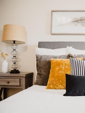 bed with pillows, nightstand with glass table lamp and art over bed
