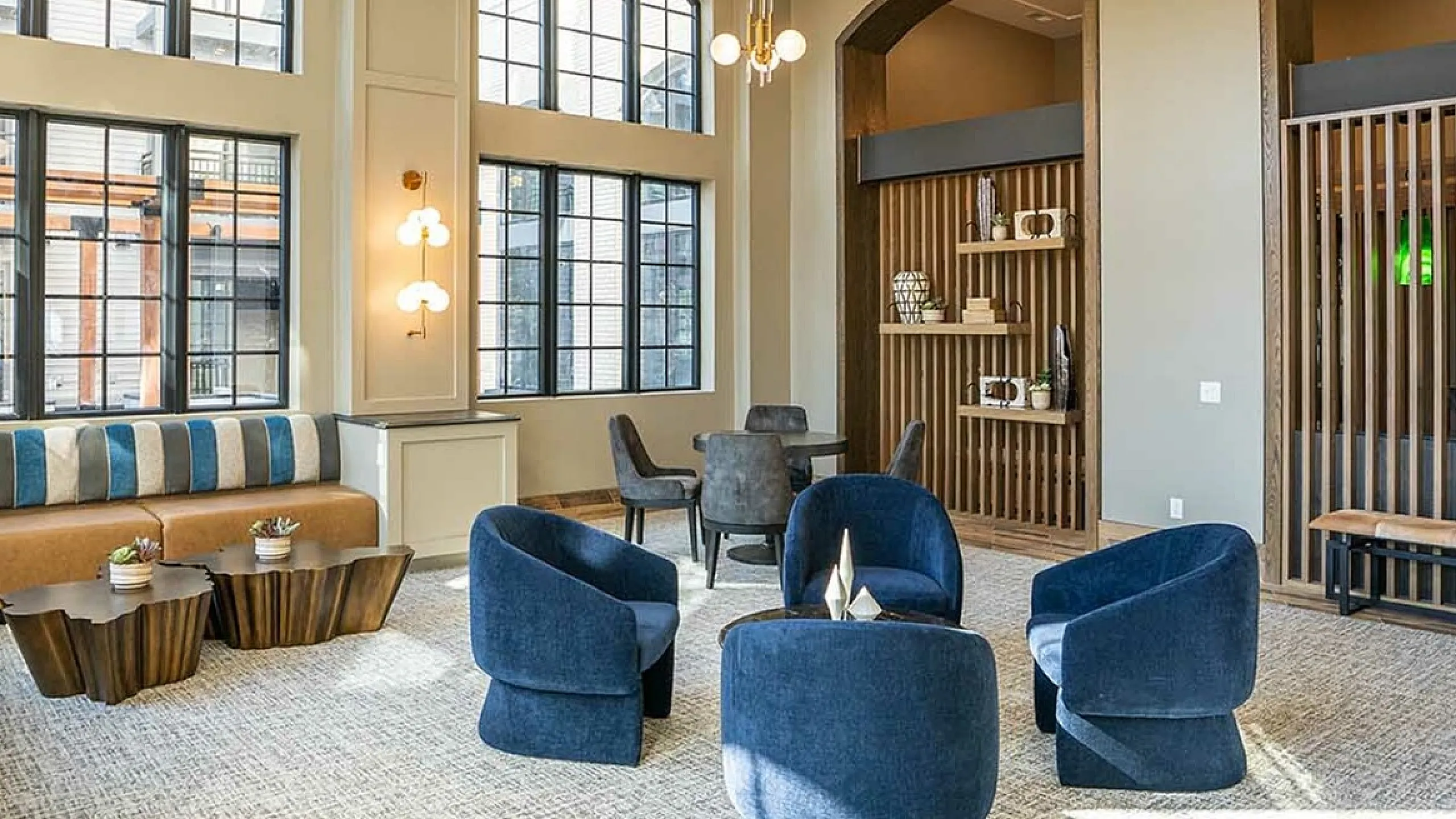 Spacious lounge with modern decor, featuring plush blue chairs, stylish lighting, and large windows.