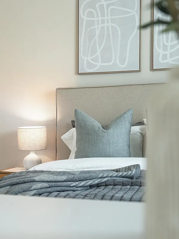 Inviting bedroom featuring a comfortable bed with soft gray linens, artistic wall decor, and a glowing bedside lamp.