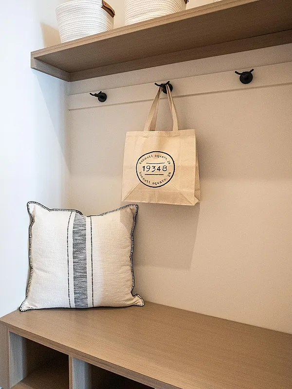 Stylish entryway with a wooden bench, decorative pillow, storage baskets, and a hanging tote bag.