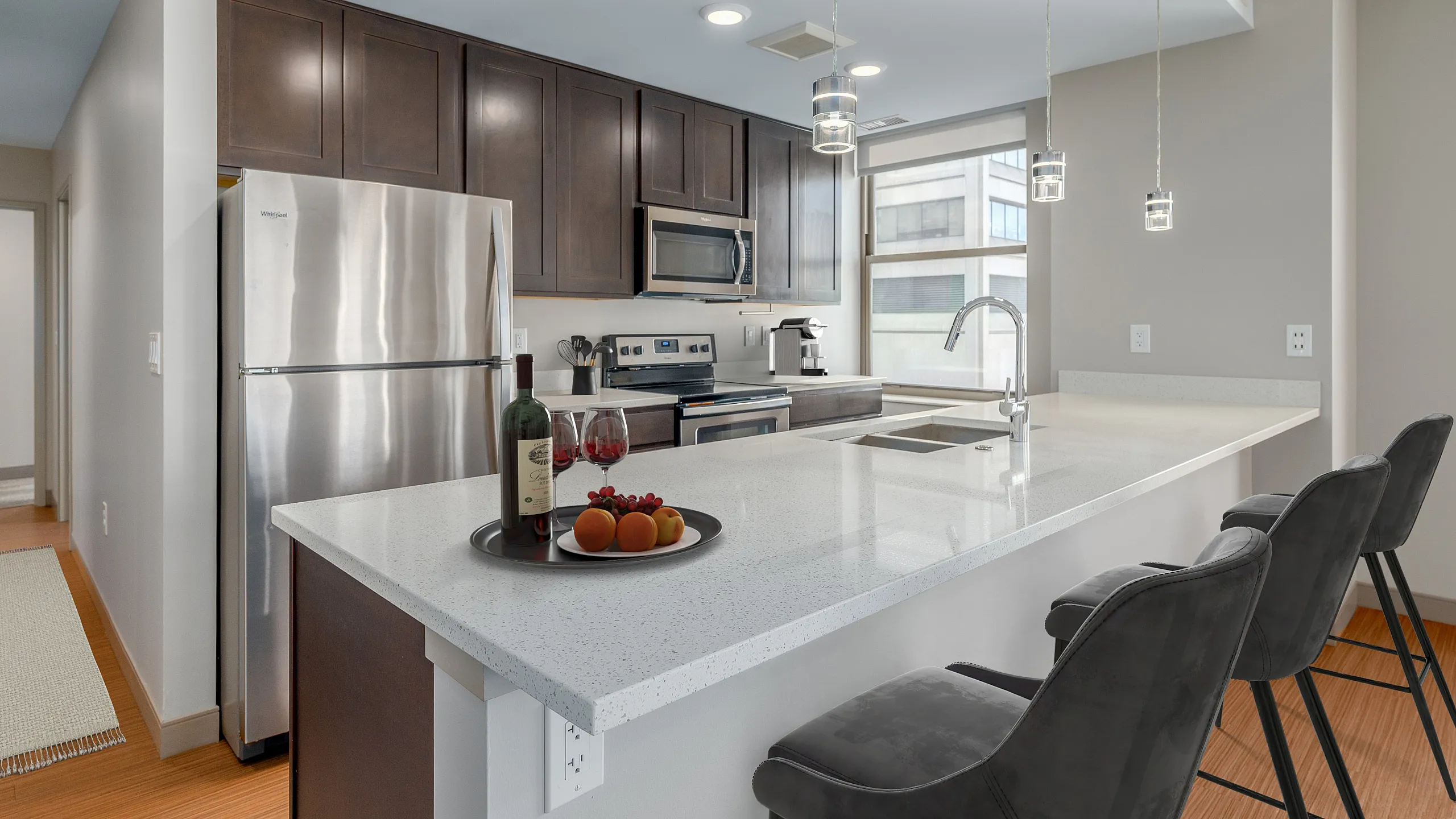 Modern kitchen with sleek stainless steel appliances, dark wood cabinets, and a spacious white countertop with stylish bar stools.
