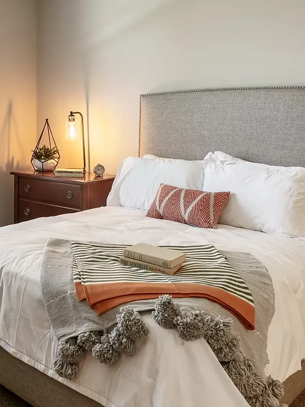 Stylish bedroom featuring a plush bed with grey pillows, modern bedside lamp, and abstract art on the wall.