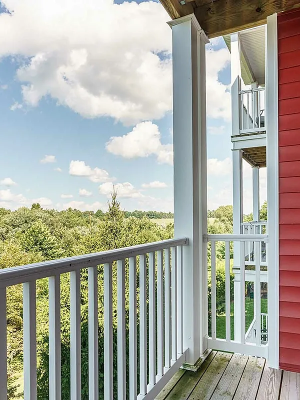 Charming balcony with white railings, red siding, and scenic view of lush green landscape.
