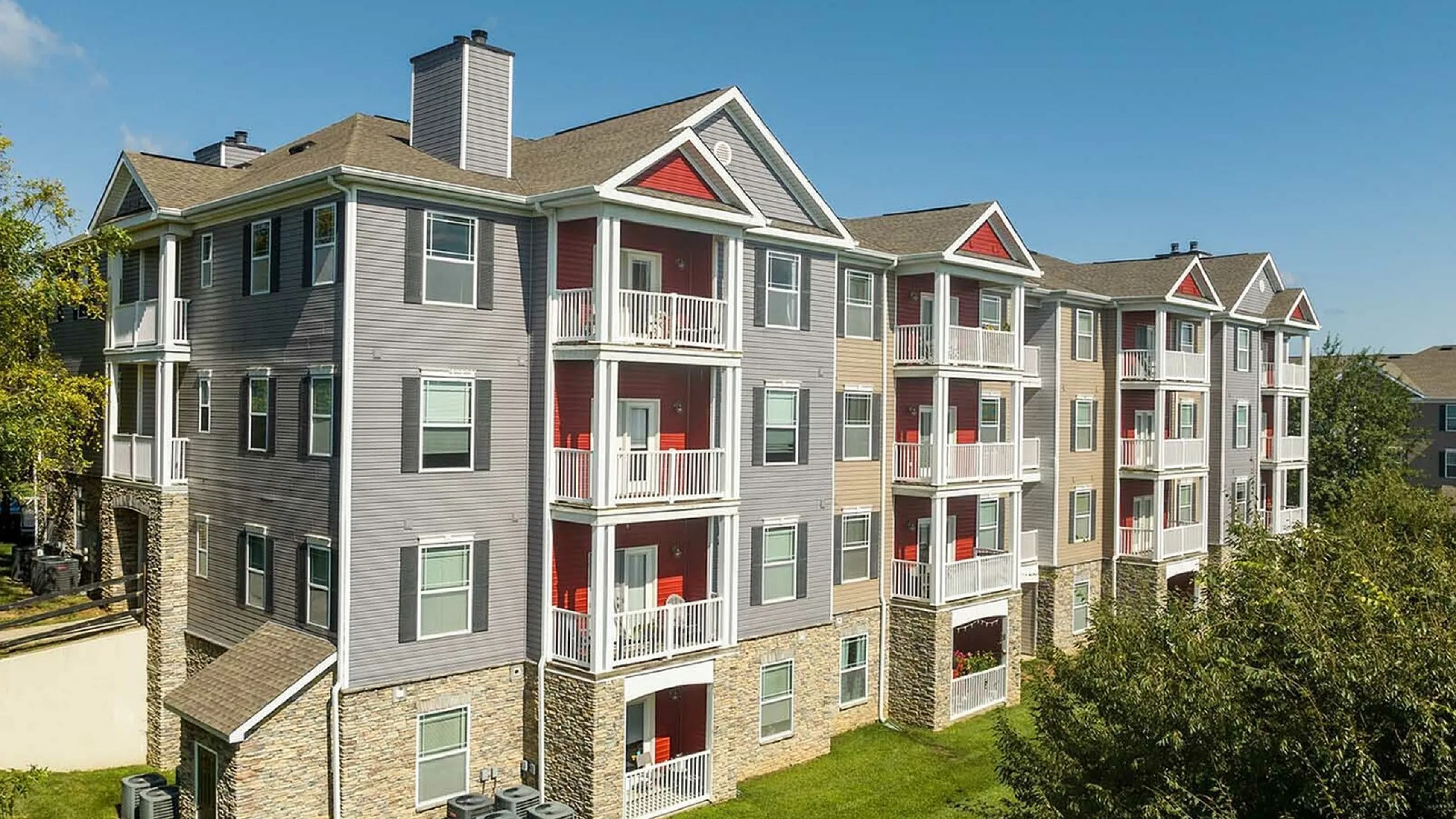 Sunlit view of a modern apartment complex with spacious balconies and lush greenery.