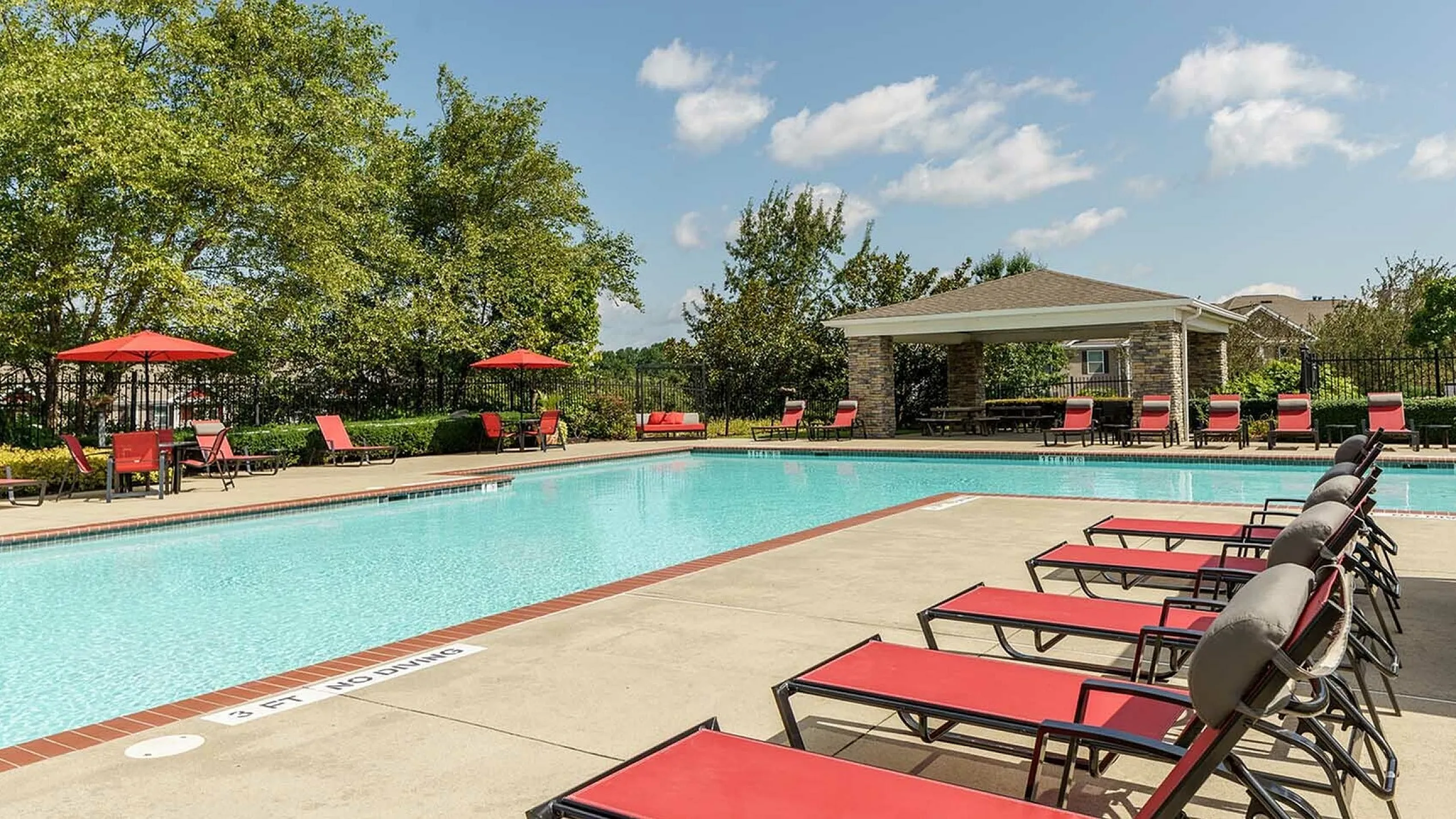 Inviting outdoor pool with red loungers, shaded patio, and lush greenery.