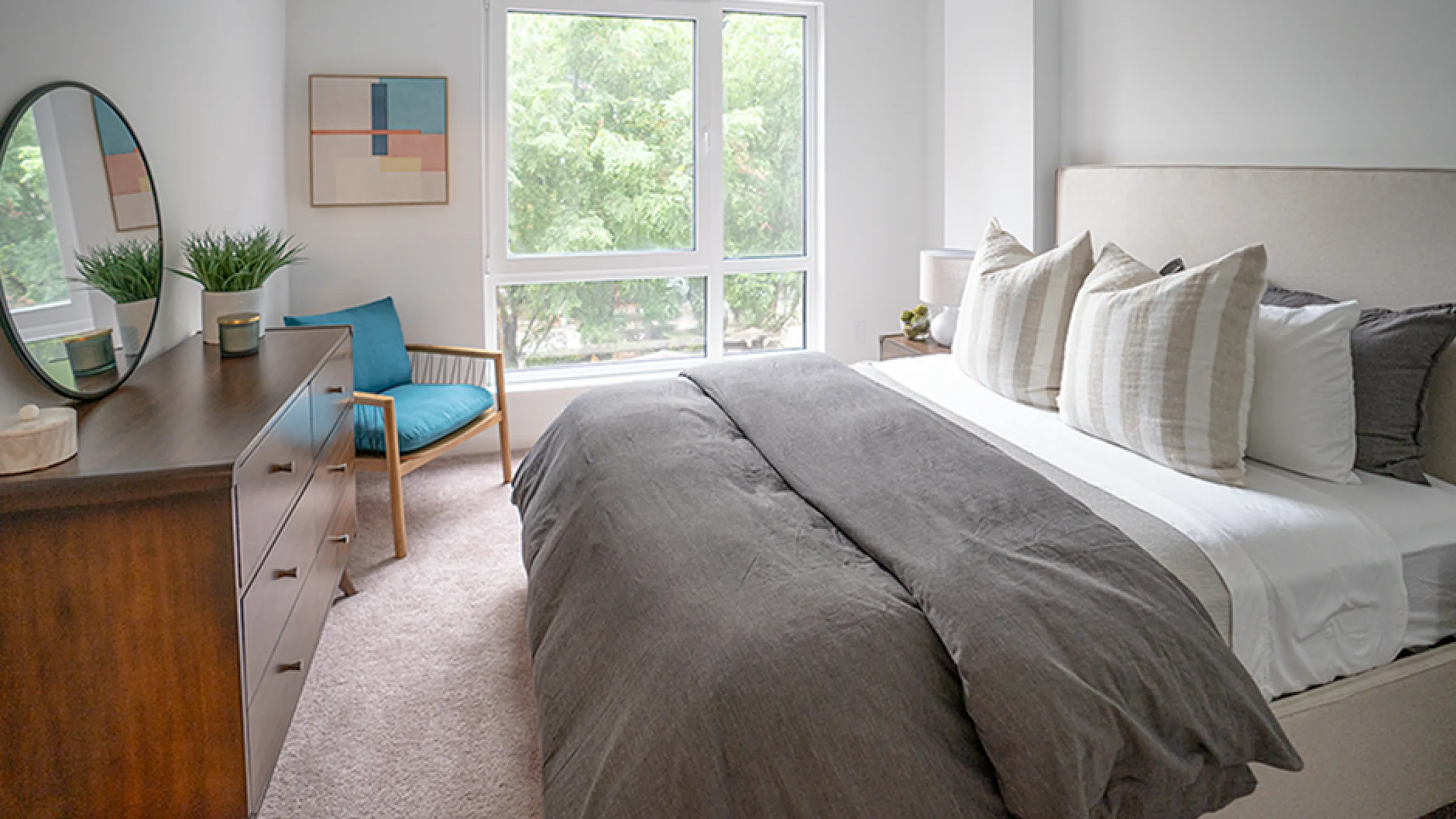 Bright and inviting bedroom with modern decor, featuring large windows, contemporary artwork, and a cozy armchair.