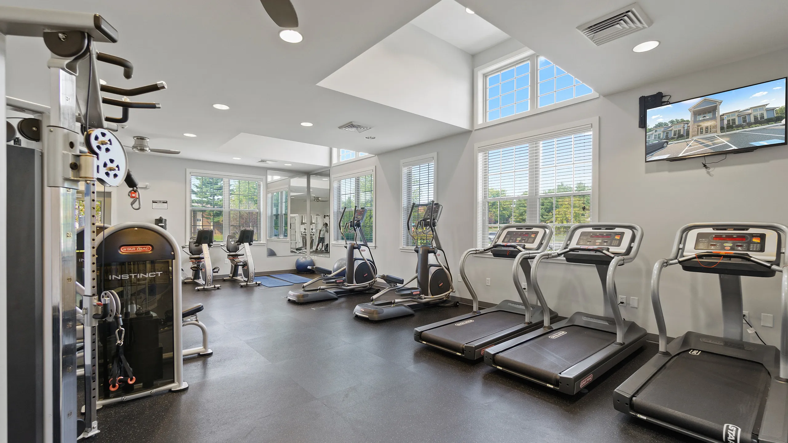 Bright and modern gym with state-of-the-art equipment, including treadmills, elliptical machines, and weight lifting station, featuring large windows for natural light.