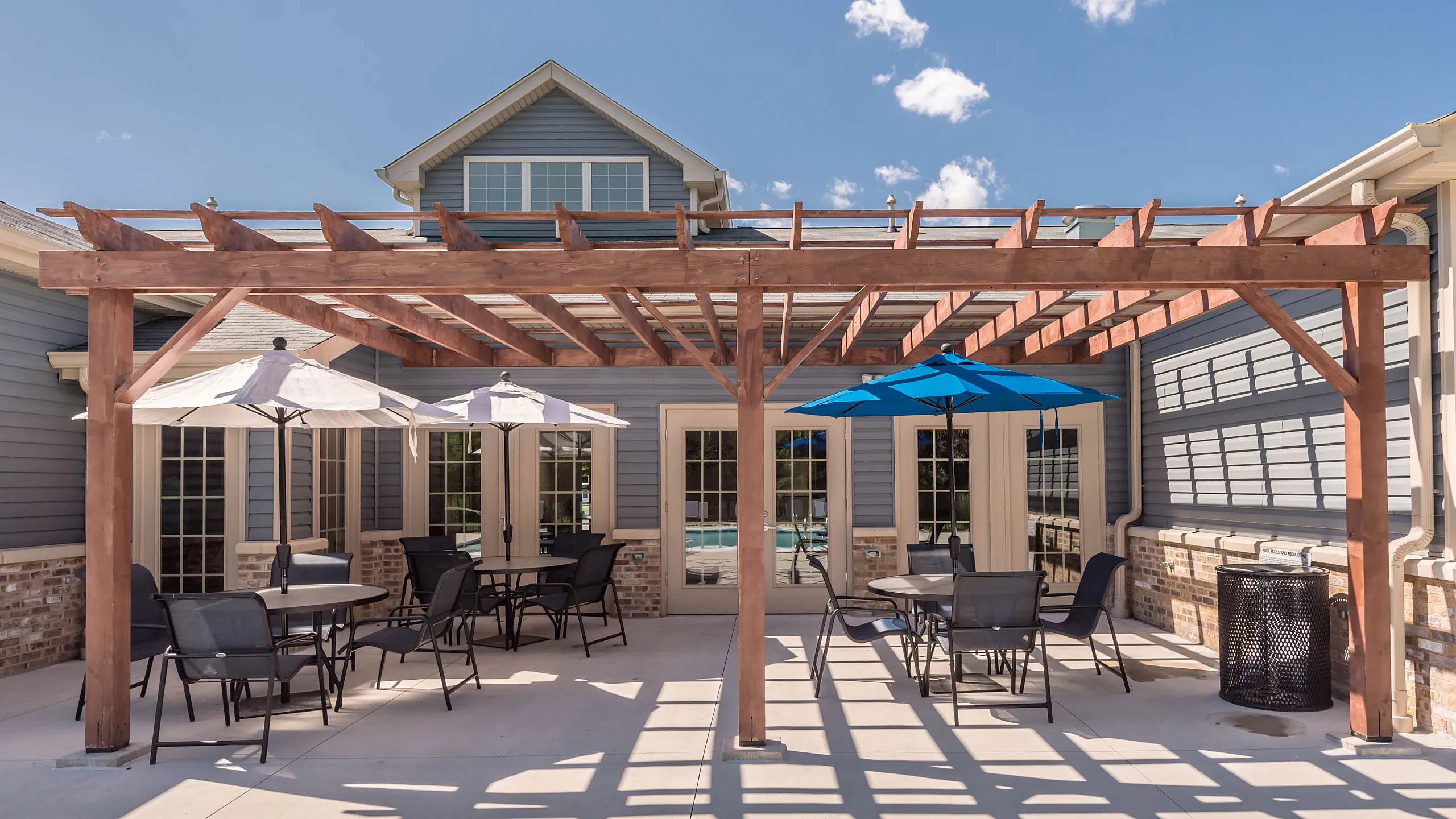 Elegant outdoor patio featuring a wooden pergola, modern seating, and vibrant umbrella shades, perfect for relaxation and entertainment.