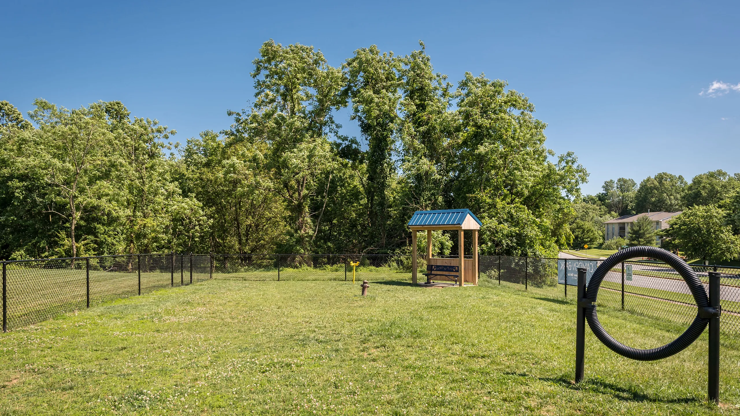 Charming fenced green space featuring a cozy gazebo and scenic tree-lined backdrop, perfect for relaxation and recreation.