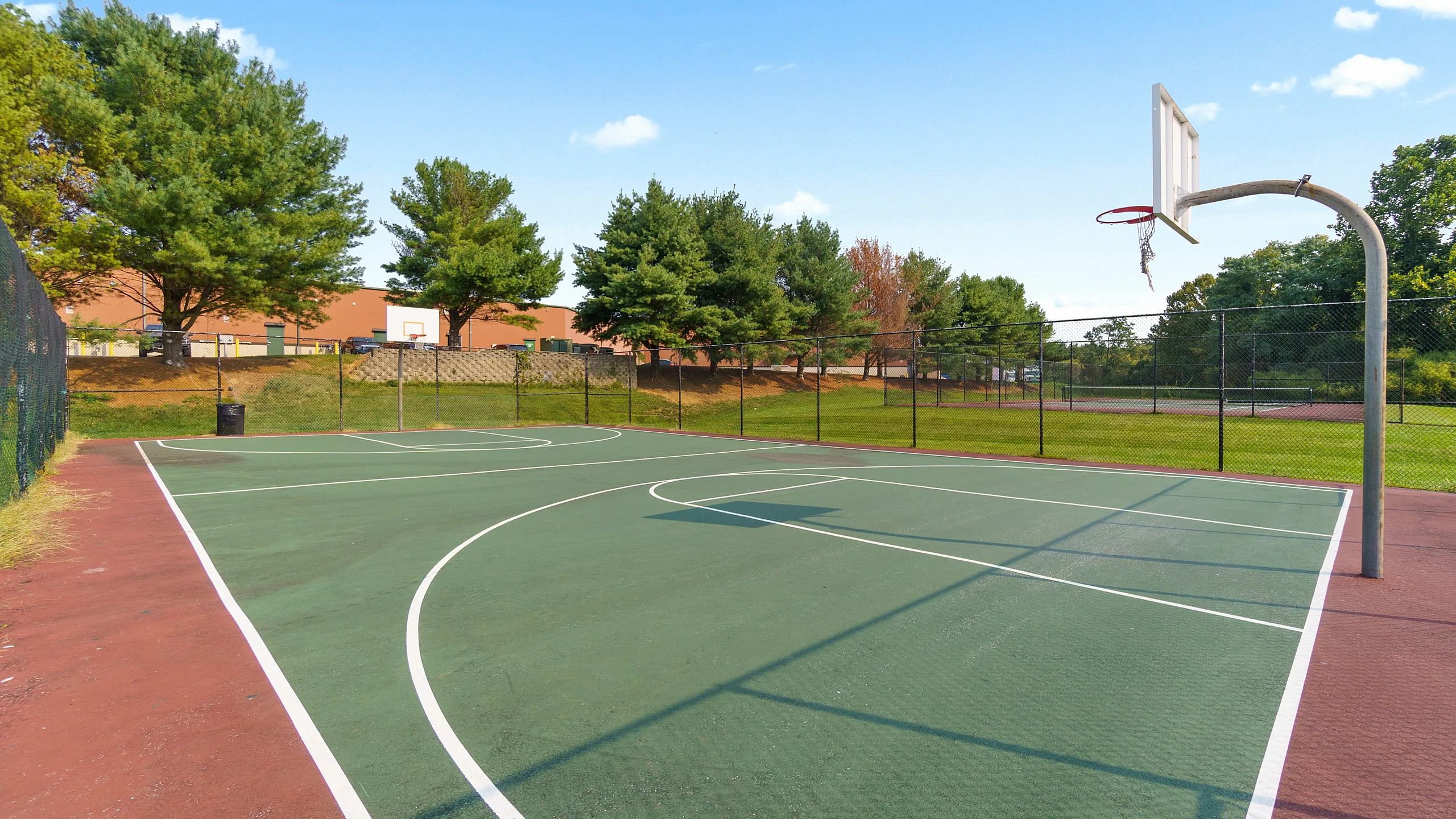 Inviting outdoor basketball court surrounded by lush green trees, perfect for recreation and exercise in a serene setting.