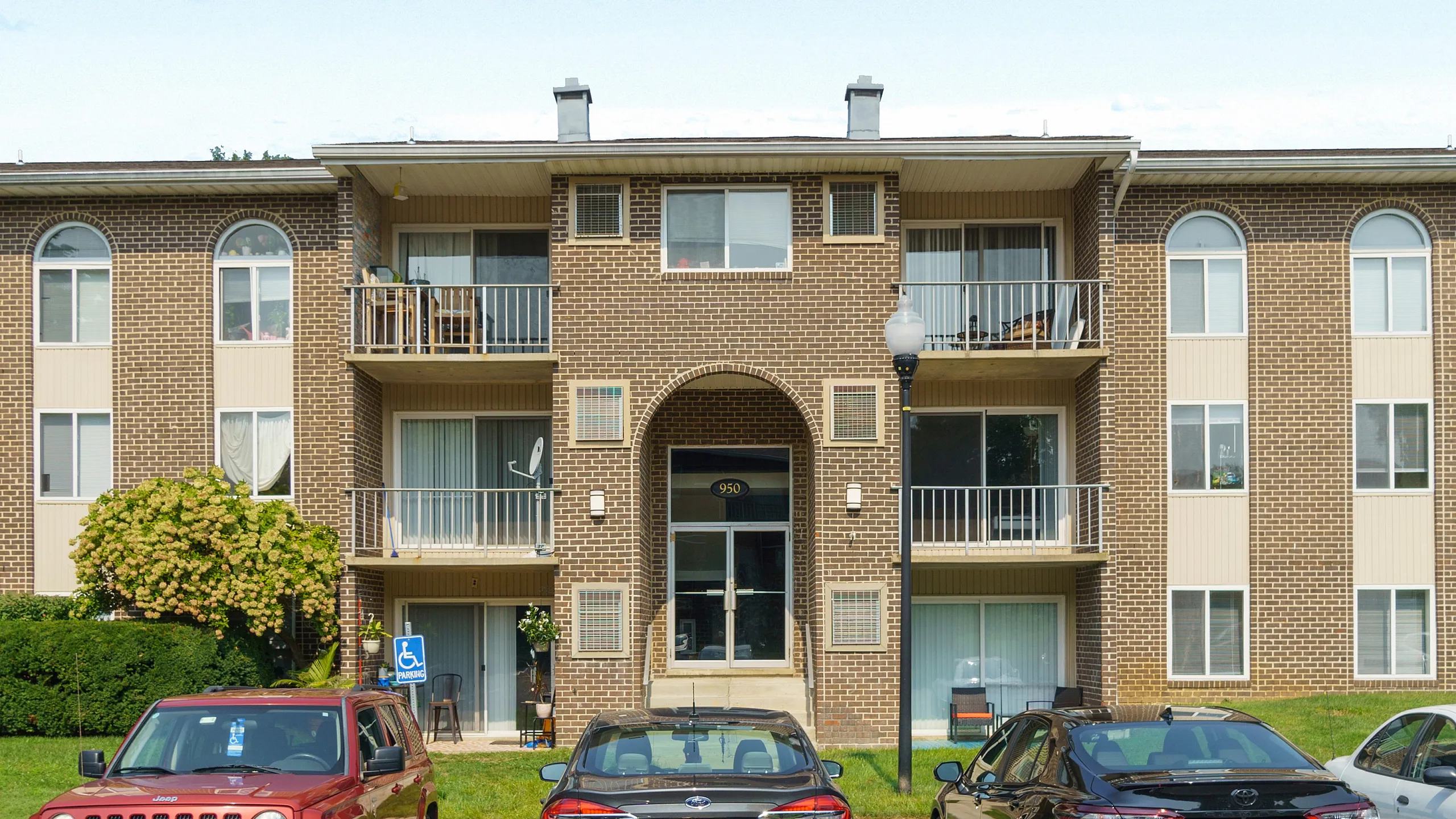 Charming brick apartment building with balconies and reserved parking, surrounded by lush greenery.