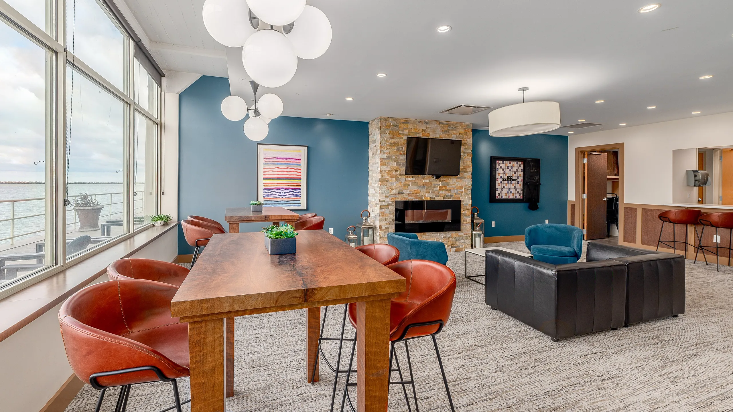 Luxurious waterfront lounge with modern lighting, stylish seating, and a chic stone fireplace, offering stunning lake views.