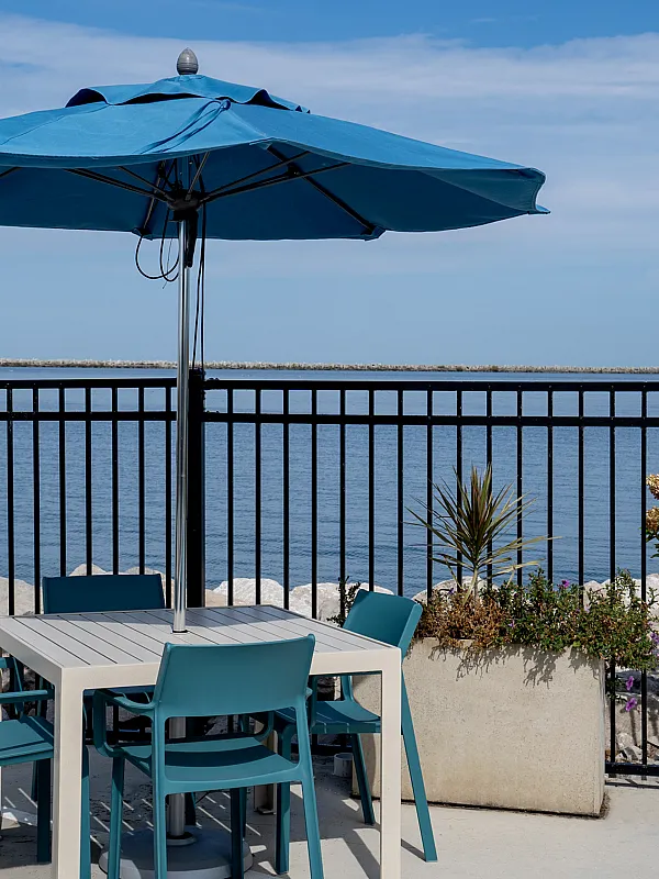 Charming seaside patio setup with a modern table and chairs under a blue umbrella, offering serene ocean views.