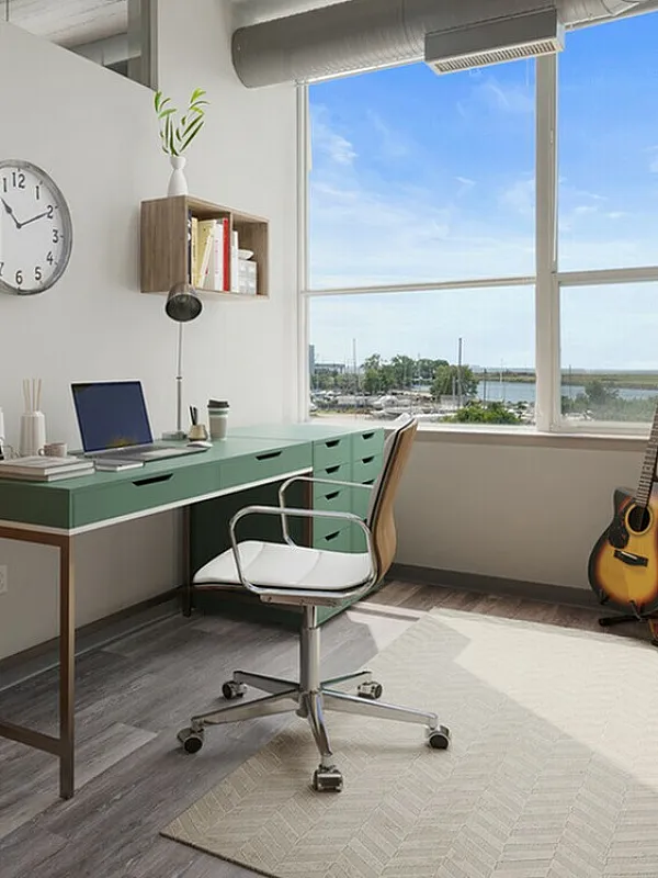 Bright and modern home office with a green desk, floor-to-ceiling window, cozy couch, and stylish decor, offering a stunning view of the waterfront.