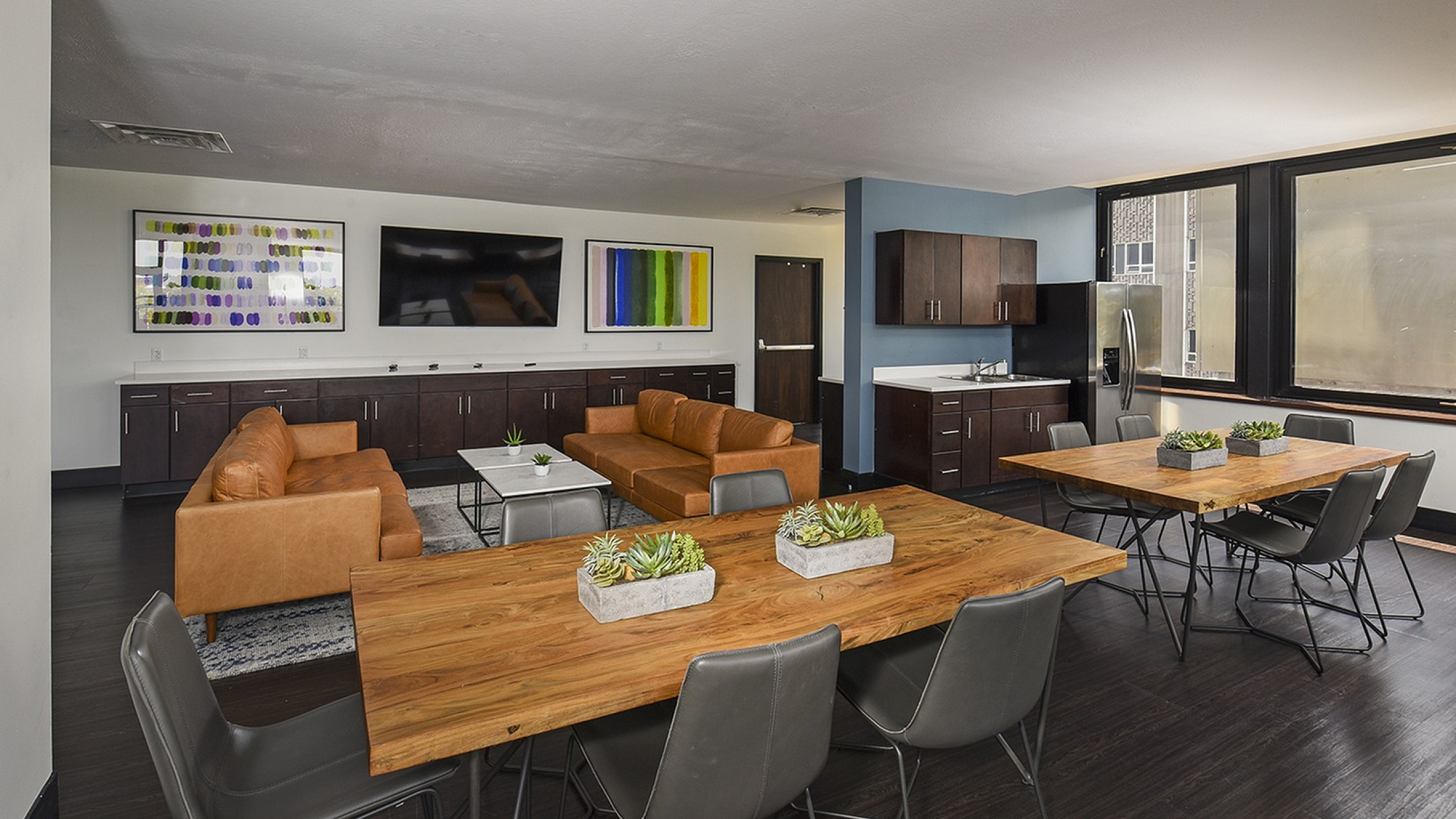 Inviting communal lounge boasting elegant wooden tables, cozy leather sofas, and a sleek kitchenette, ideal for social gatherings.