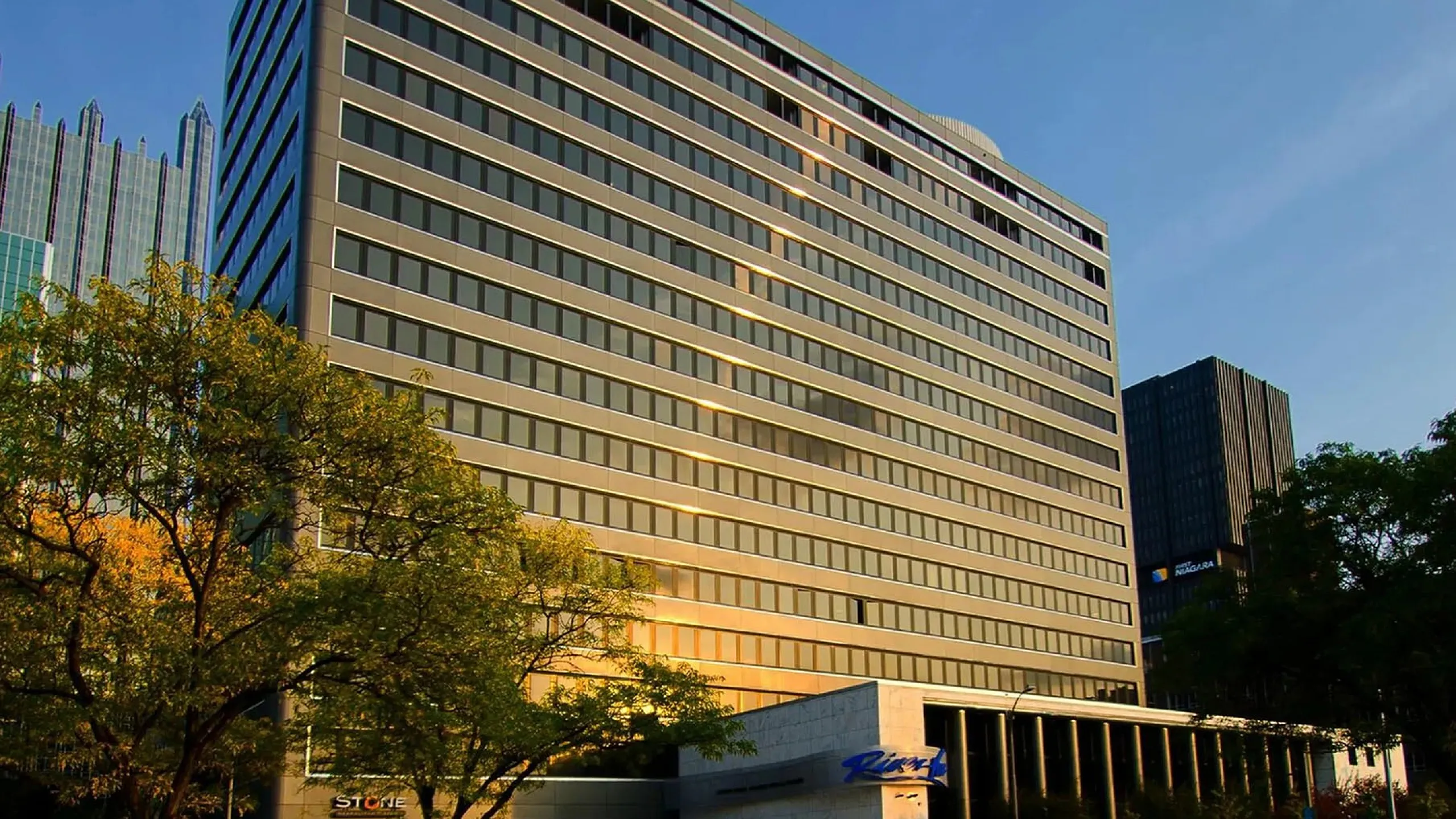 Impressive multi-story office building with a modern design, featuring large windows and surrounded by lush greenery, basking in warm sunlight.