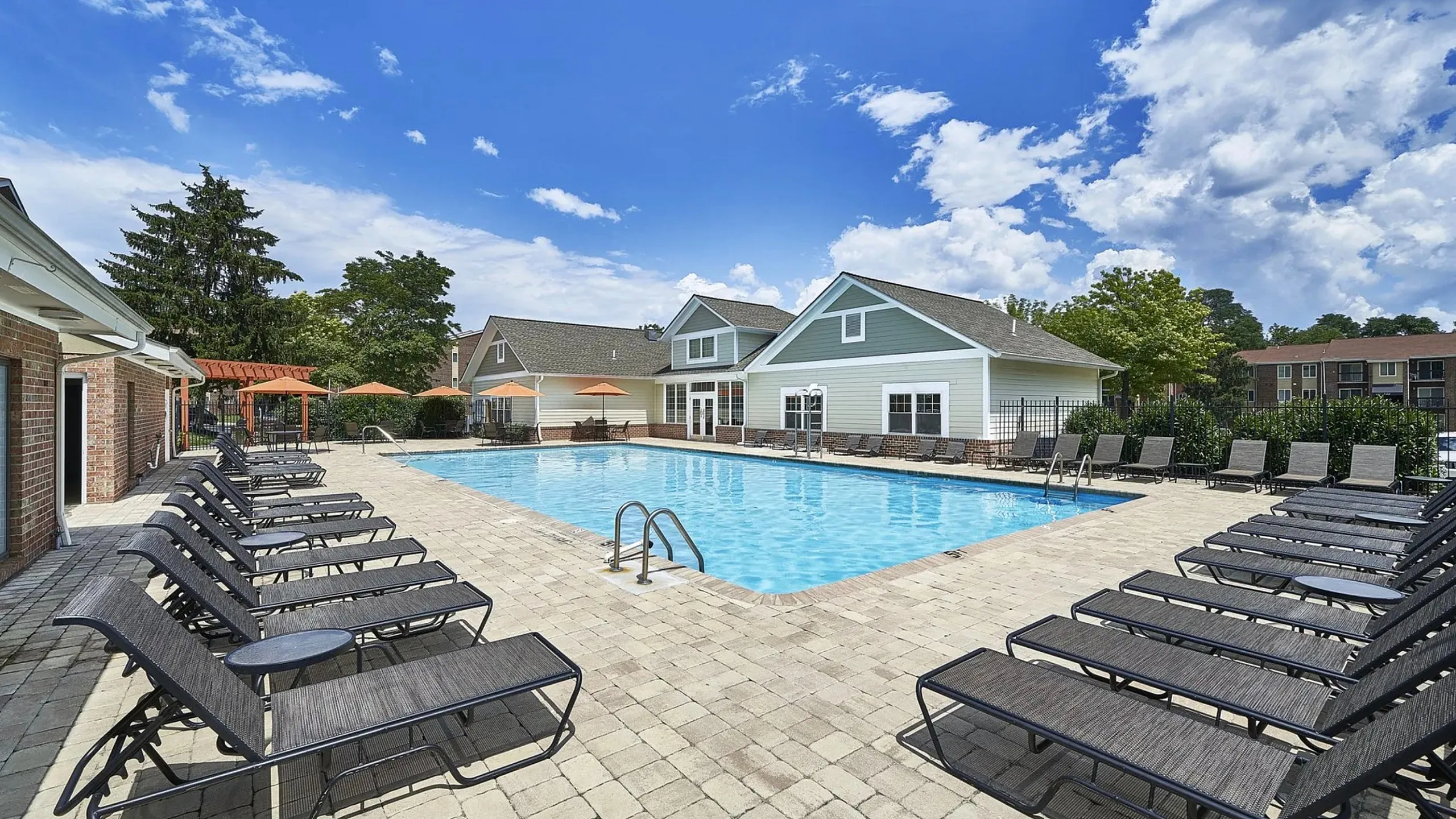 Inviting community pool area with modern lounge chairs and scenic views, perfect for relaxation under a bright blue sky.