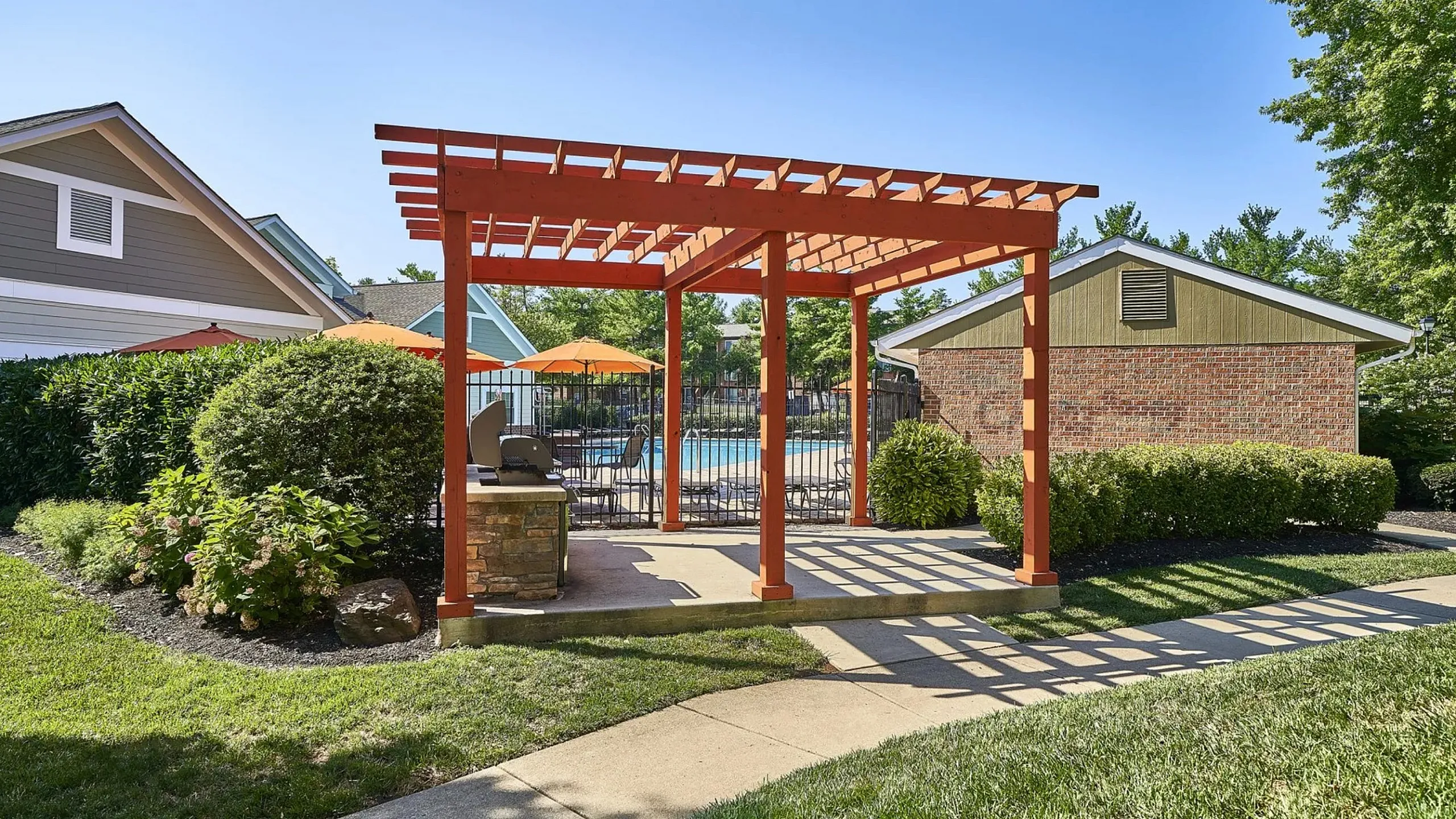 Inviting outdoor space featuring a pergola, lush greenery, and a view of the sunlit swimming pool area.