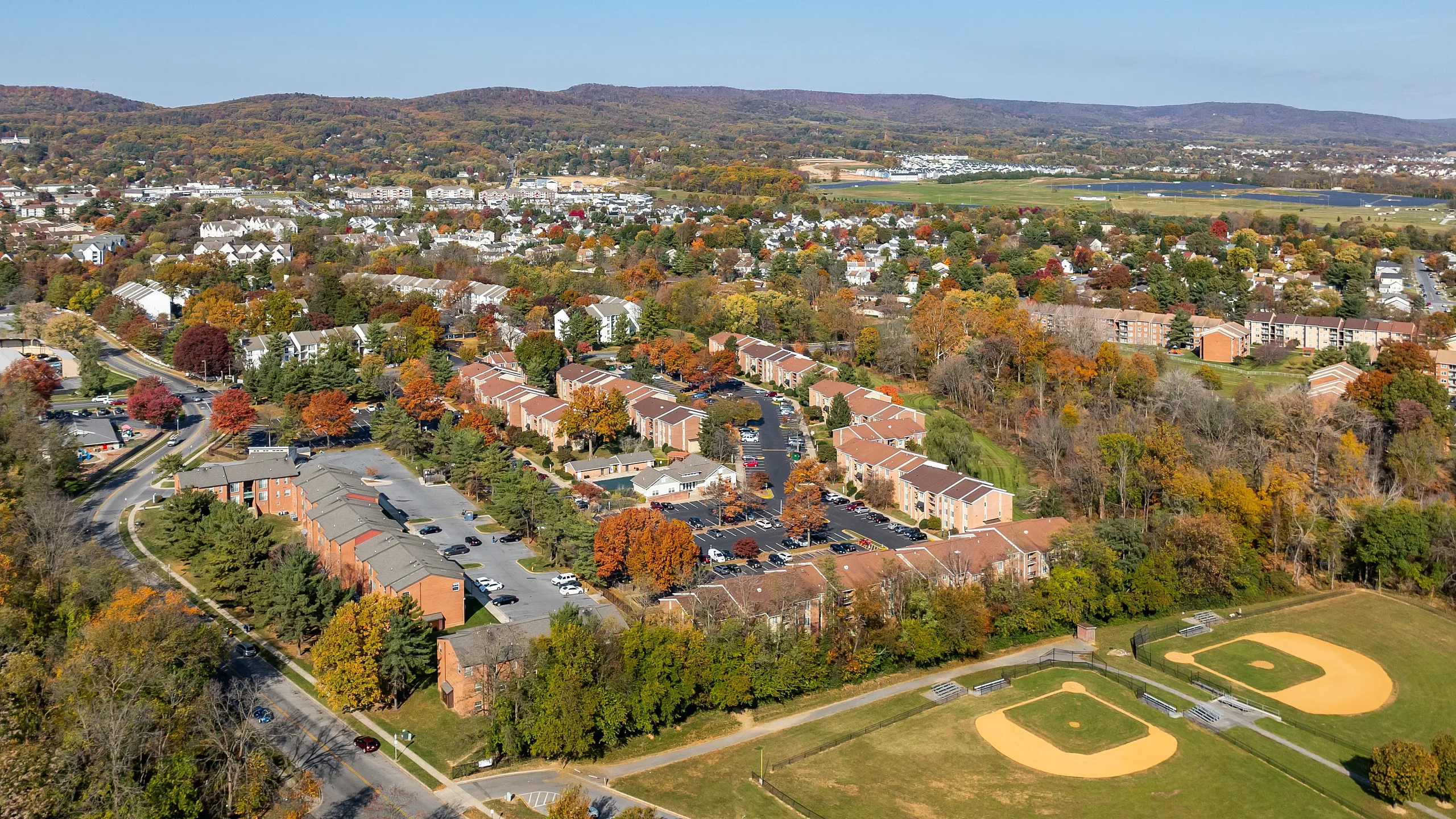 Scenic aerial view of charming suburban neighborhood with vibrant autumn foliage, nestled alongside lush parks and well-designed sports fields.