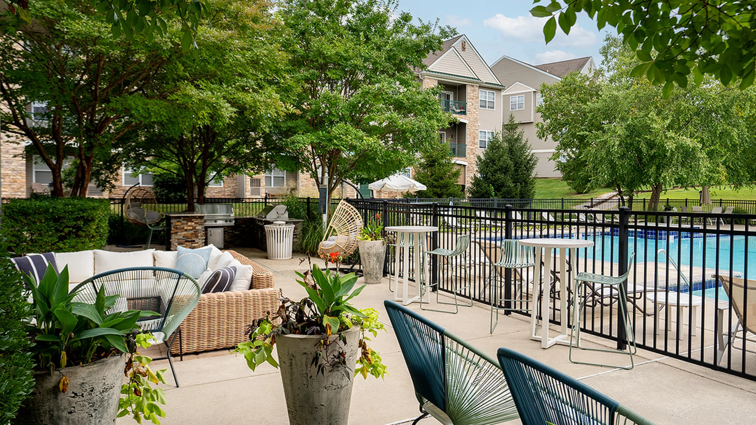 Inviting outdoor patio with lush greenery, modern seating, and poolside view in a serene apartment setting.