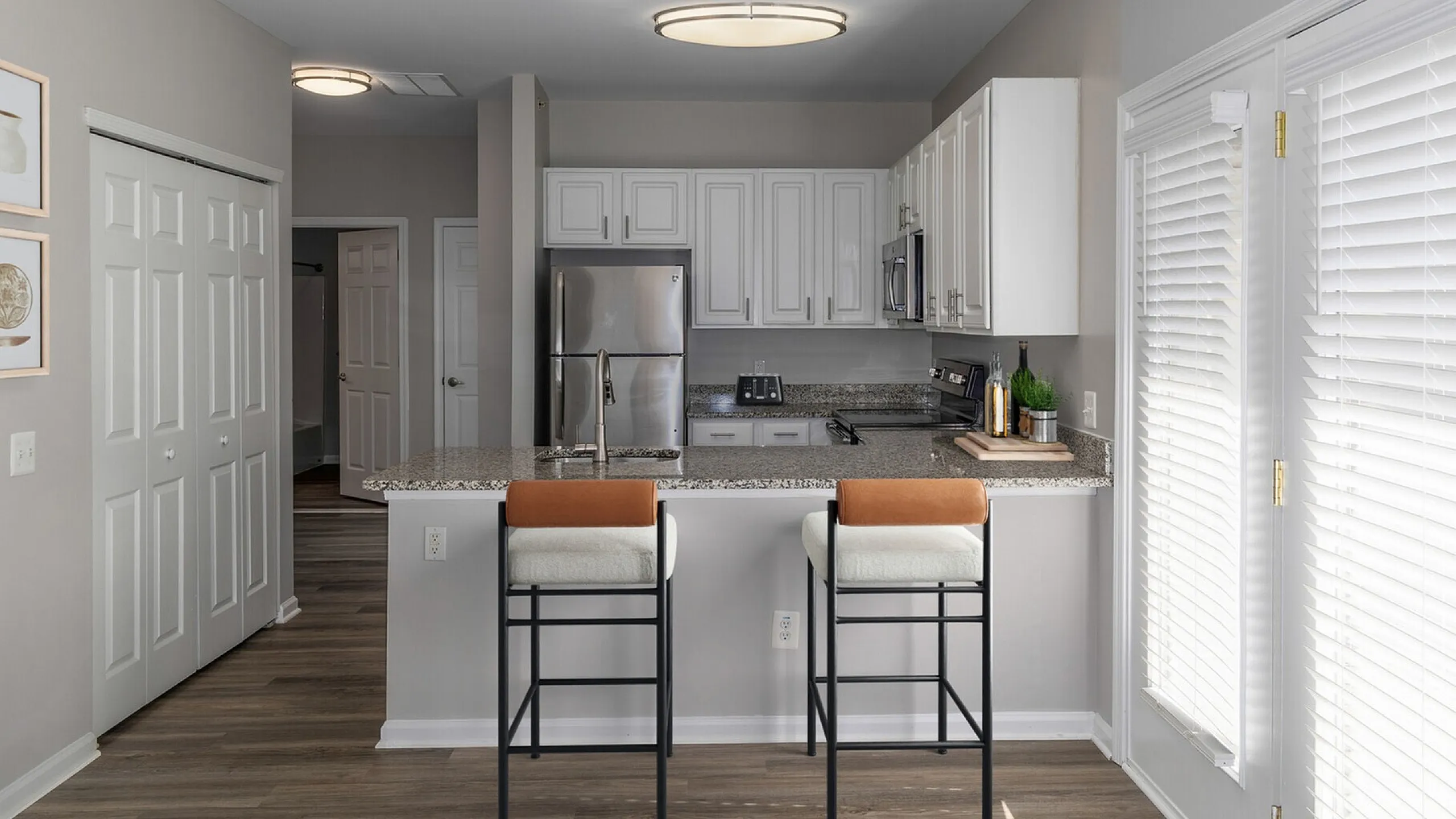 Modern kitchen with sleek granite countertops, stainless steel appliances, and chic bar stools, illuminated by natural light.