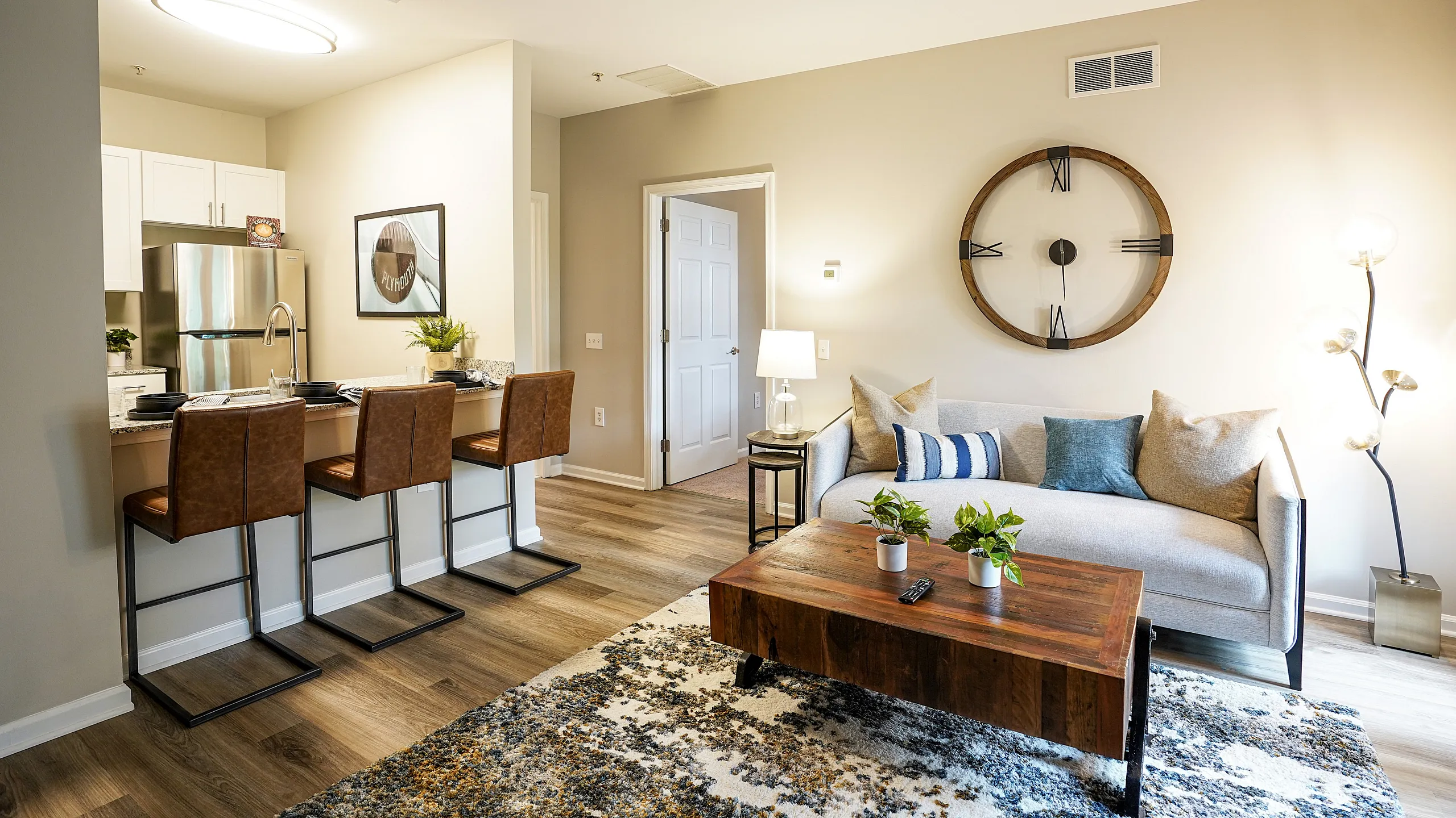 Modern living room with elegant decor, featuring a cozy sofa, rustic wooden coffee table, stylish bar stools, and contemporary kitchen in open-concept design.