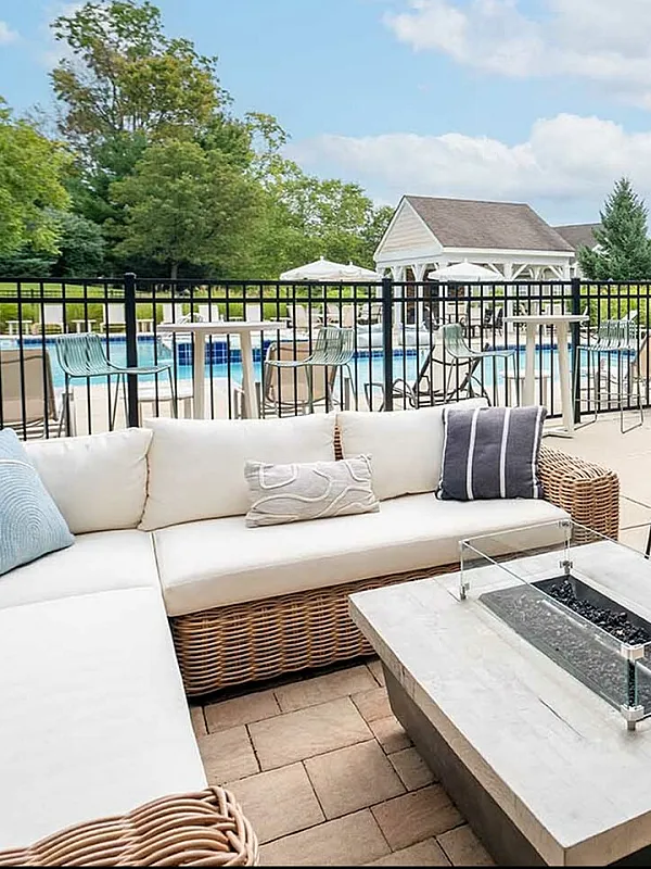 Elegant outdoor lounge area with modern seating and a cozy fire pit, overlooking a sparkling pool and lush green garden.
