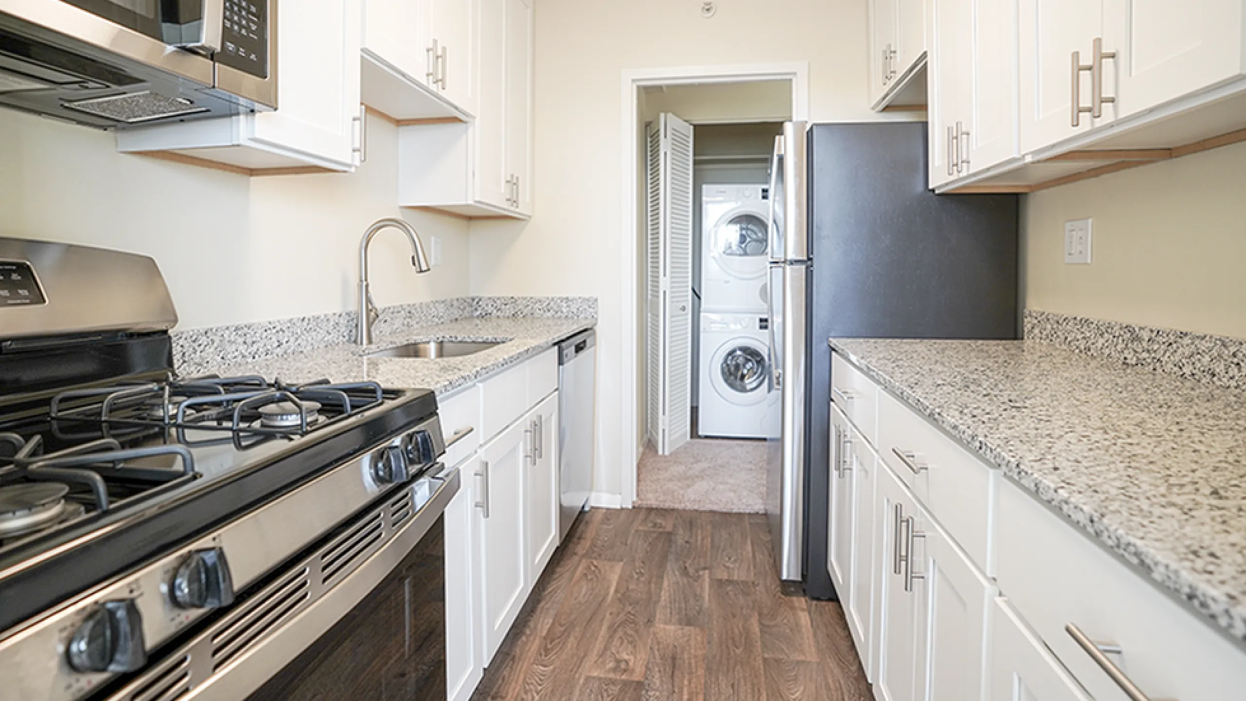 Modern galley kitchen with sleek granite countertops, stainless steel appliances, and in-unit washer-dryer.